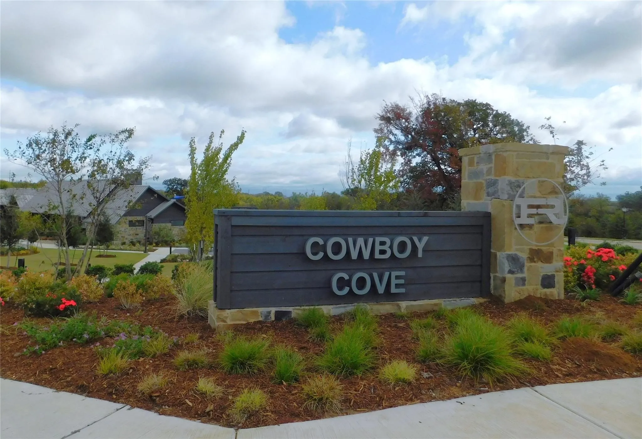 Stone and wood-finish entry monument featuring custom lettering, an integrated logo, and surrounding landscape beds with plantings and mulch