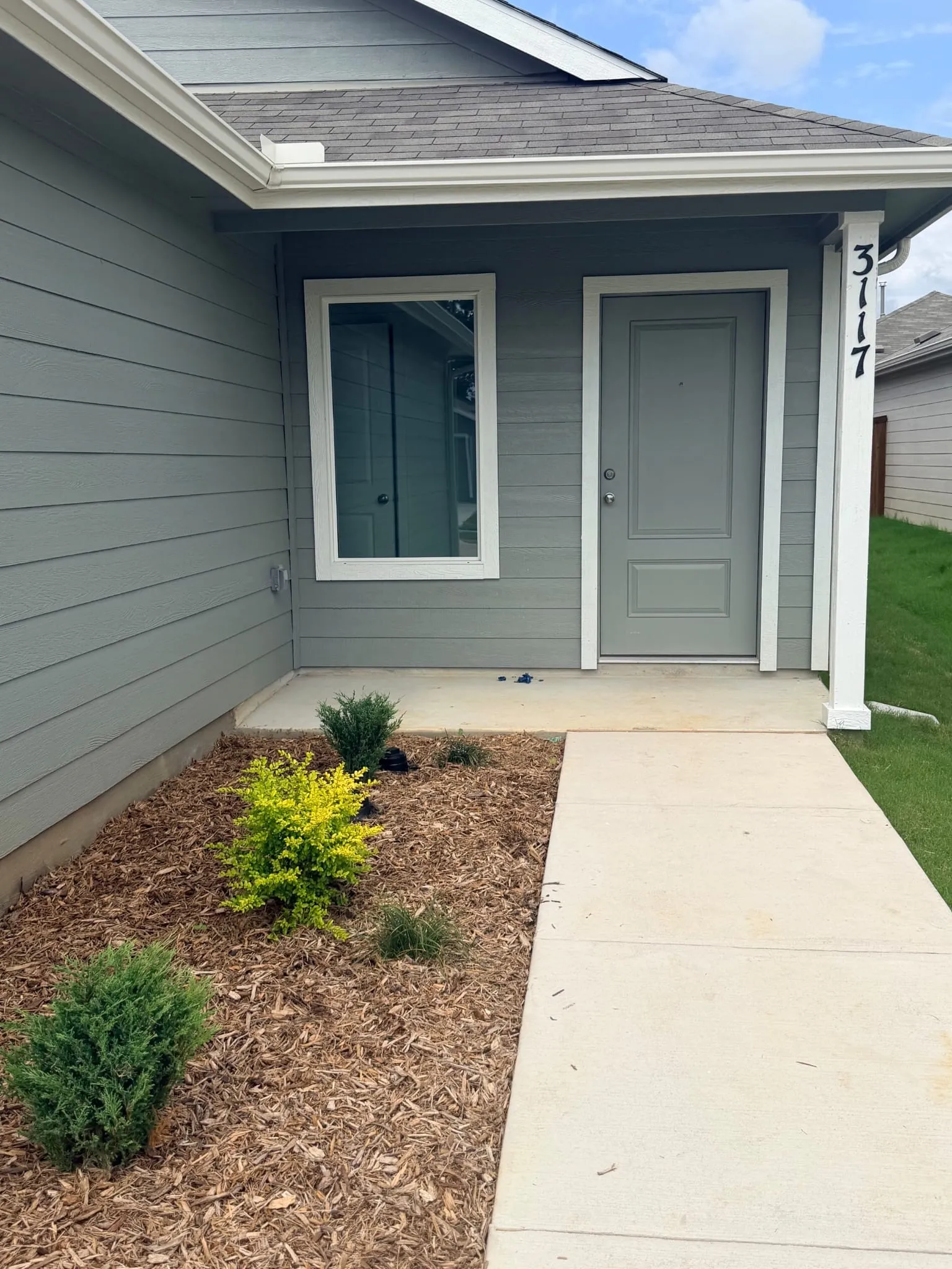 Exterior entry with gray siding and a gray door, featuring a white trim around the door and window