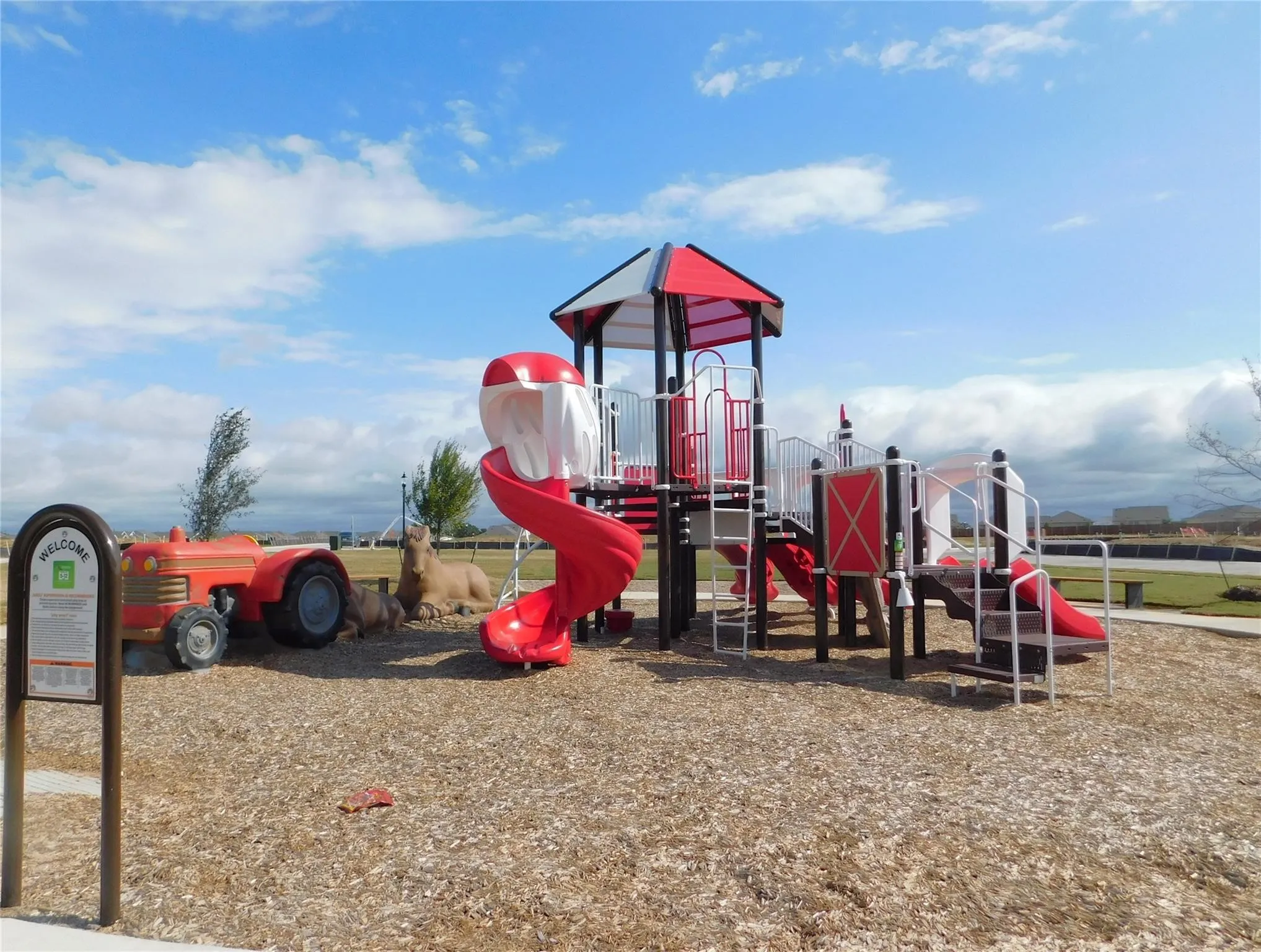Community playground featuring a multi-level play structure with red and white slides, stairs, and a covered platform