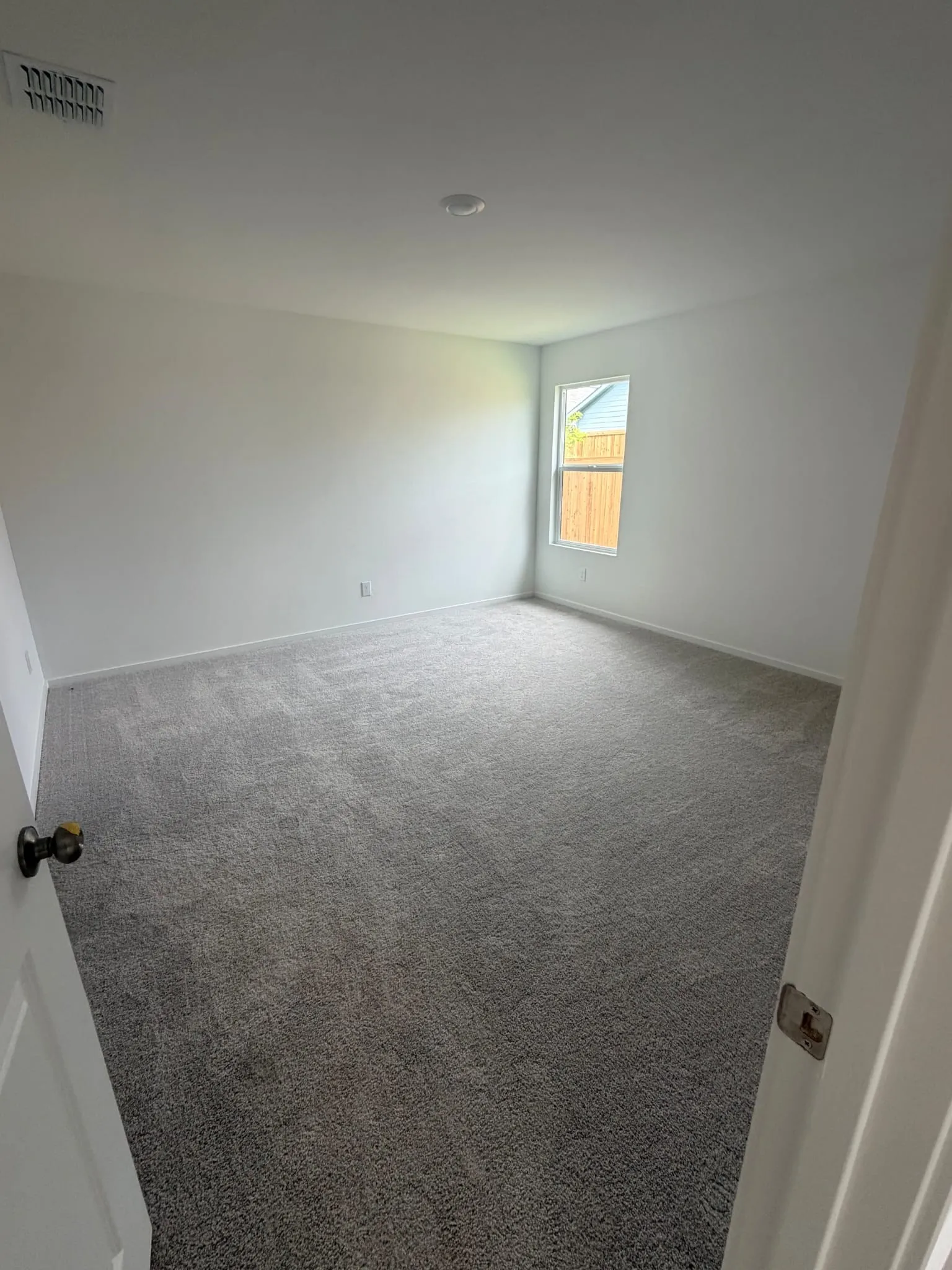 Spacious room featuring neutral carpeting, white painted walls, a recessed ceiling light, and a single window offering natural illumination
