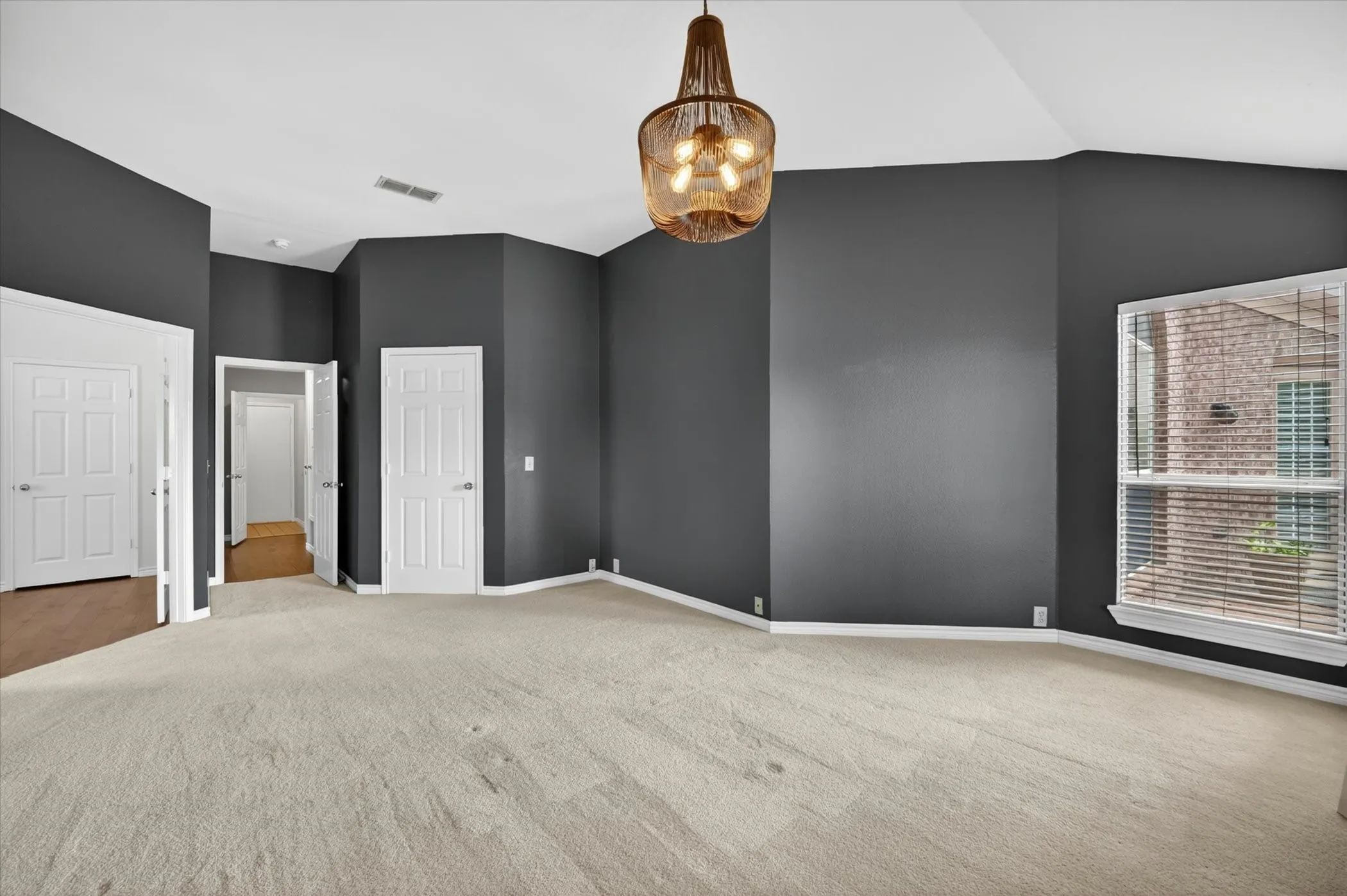 Spacious room featuring vaulted ceilings, a contemporary ceiling fixture, light-colored carpeting, multiple paneled doors, and a bay window with blinds