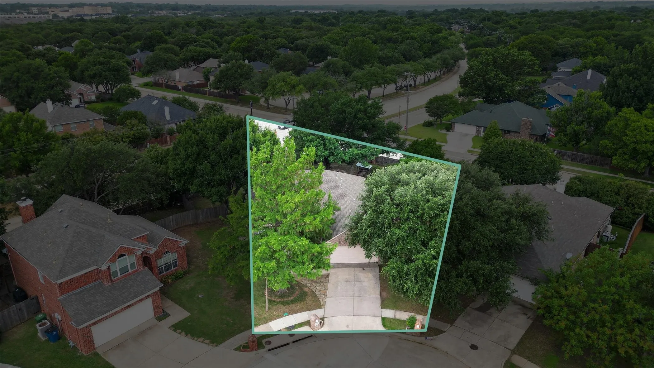 Aerial view showcasing a residential property with mature trees, a concrete driveway, and a front walkway