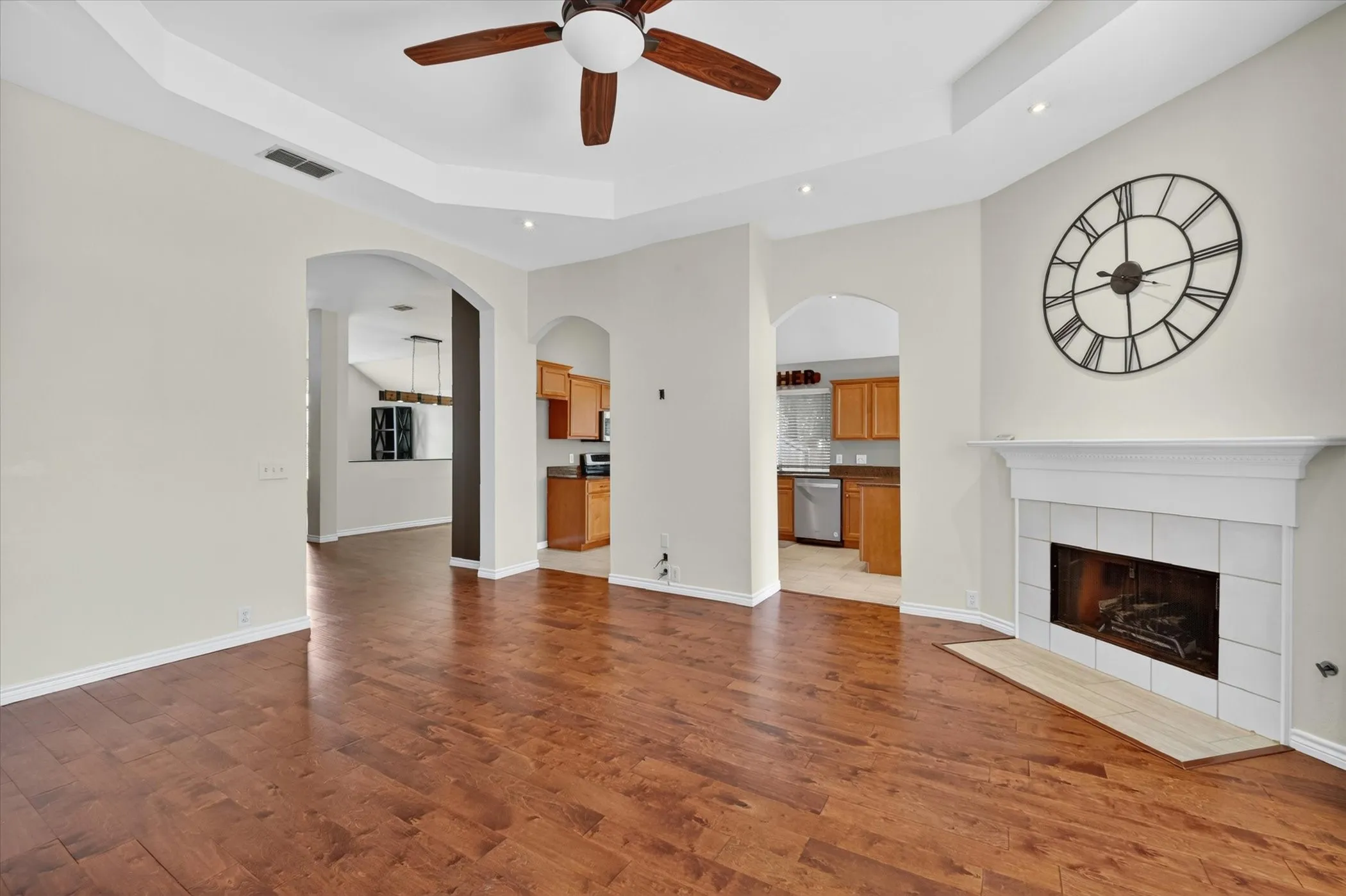 Spacious room with wood-finish flooring, a tray ceiling, and a ceiling fan