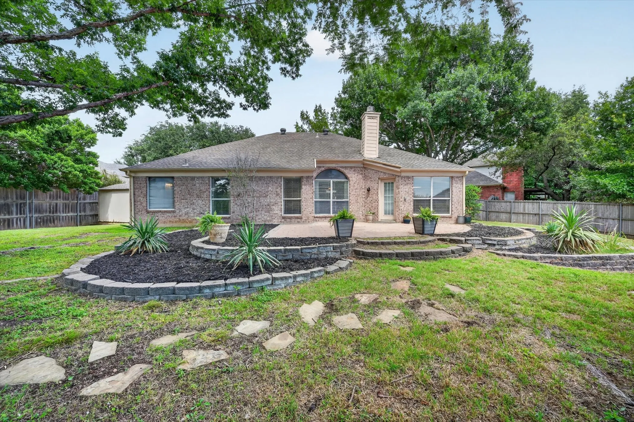 Brick exterior residence featuring a rear patio with tiered landscaping and stone steps