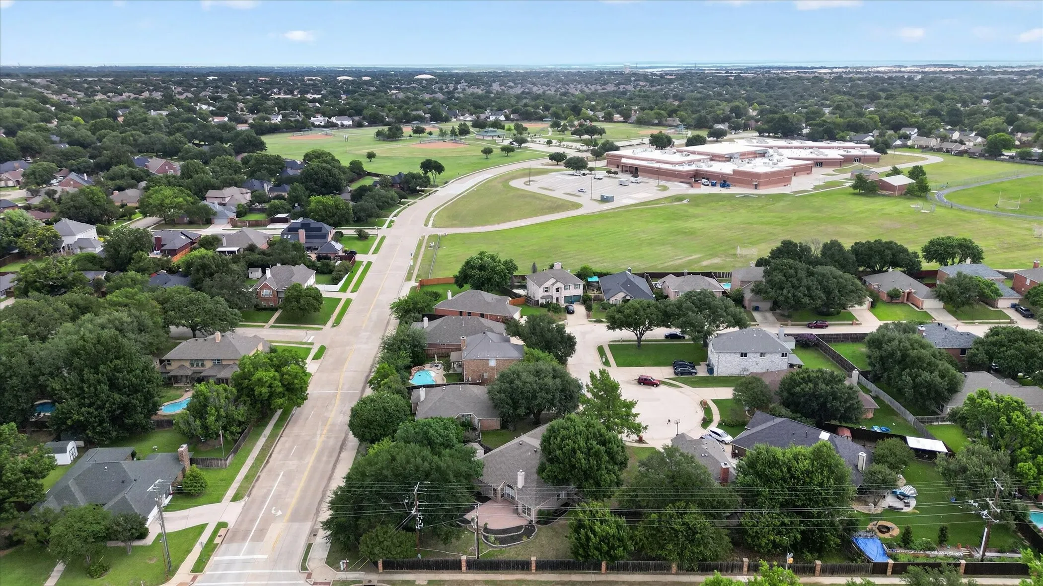 Residential neighborhood featuring mature trees, paved streets, and a nearby community building with athletic fields
