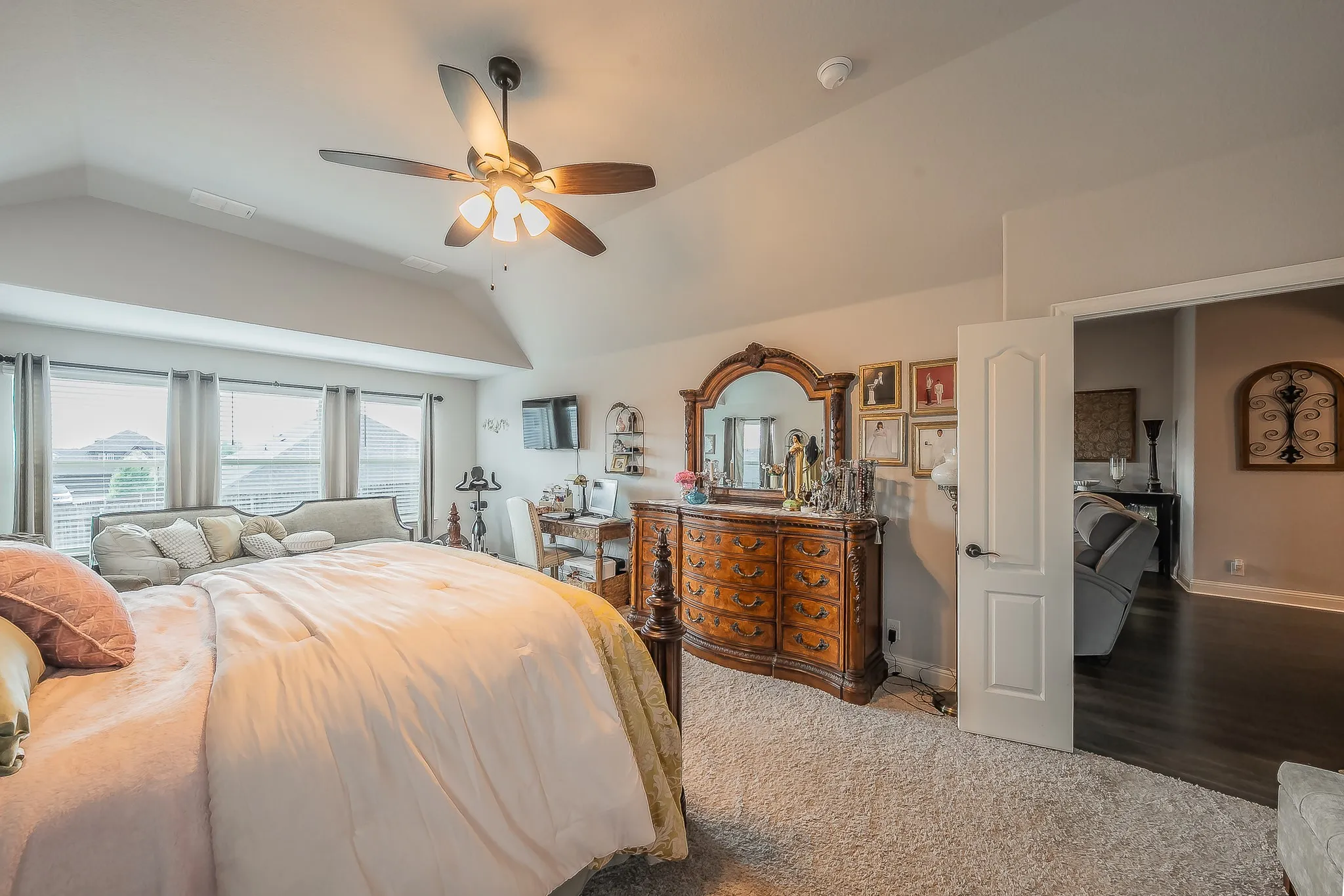 Carpeted sleeping area with vaulted ceilings, a ceiling fan with integrated lighting, and multiple windows