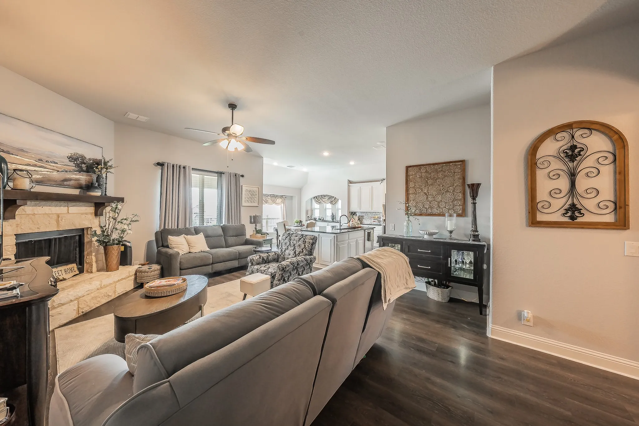 Living area featuring a stone-clad fireplace with a wood mantel, wood-finish flooring, and a ceiling fan with integrated lighting