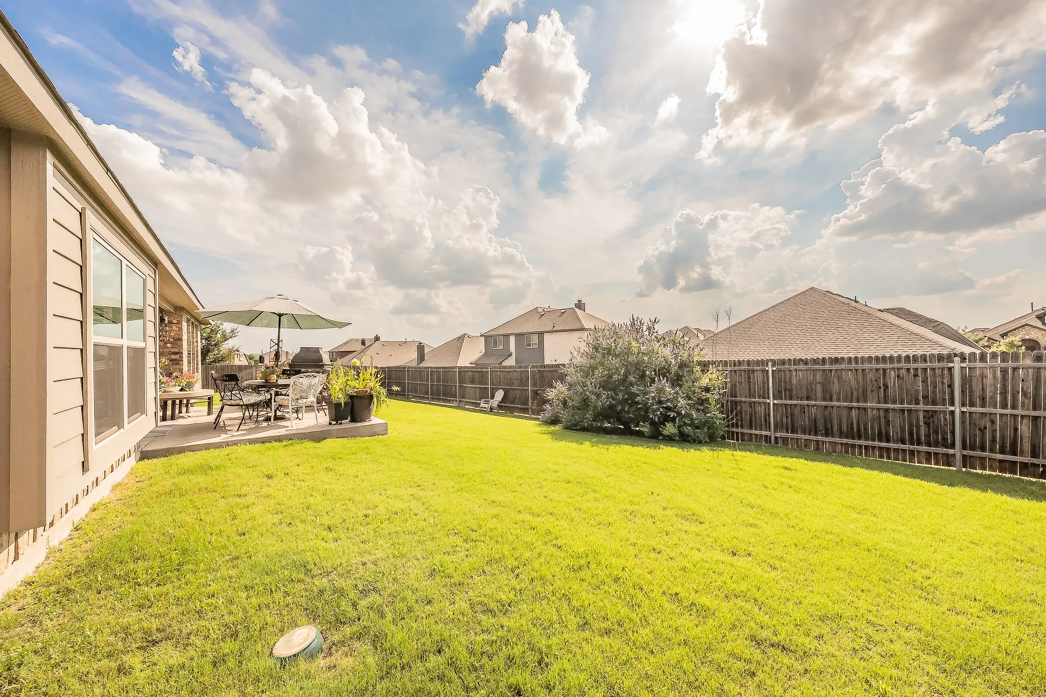 Expansive backyard featuring a manicured lawn, a full wooden privacy fence, and a concrete patio
