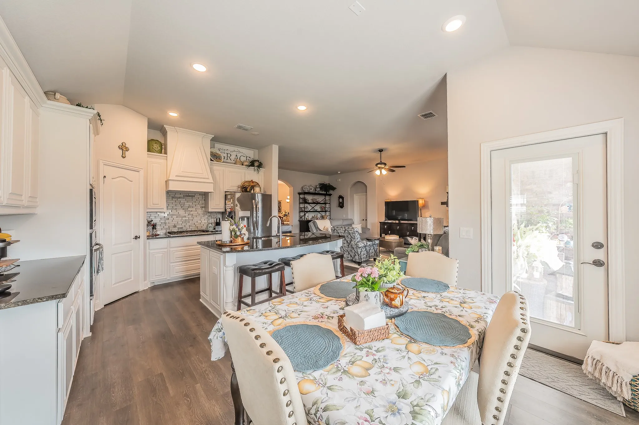 Open-concept kitchen featuring white cabinetry, dark countertops, a central island with bar seating, stainless steel appliances, and wood-finish flooring