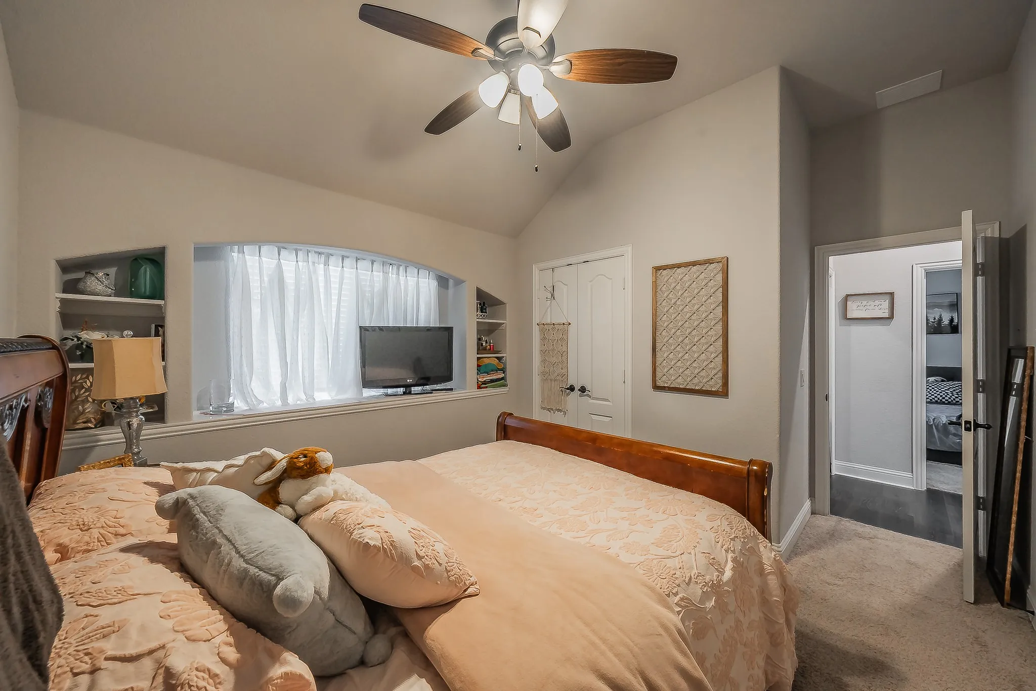 Vaulted ceiling bedroom featuring an arched window, integrated shelving, a ceiling fan, and carpet flooring