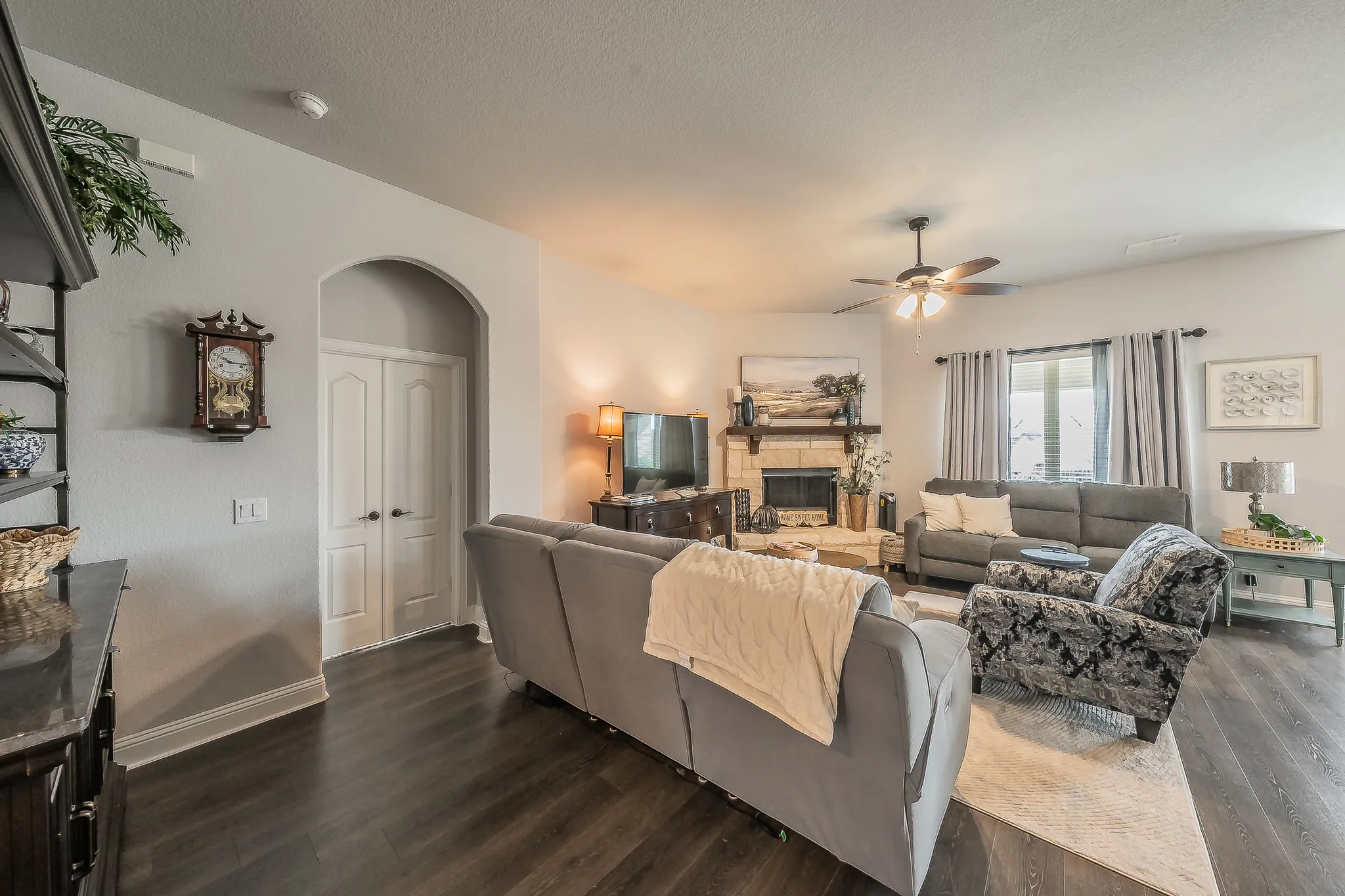 Spacious living area featuring wood-finish flooring, a stone fireplace with a mantel, an arched doorway, and white double doors