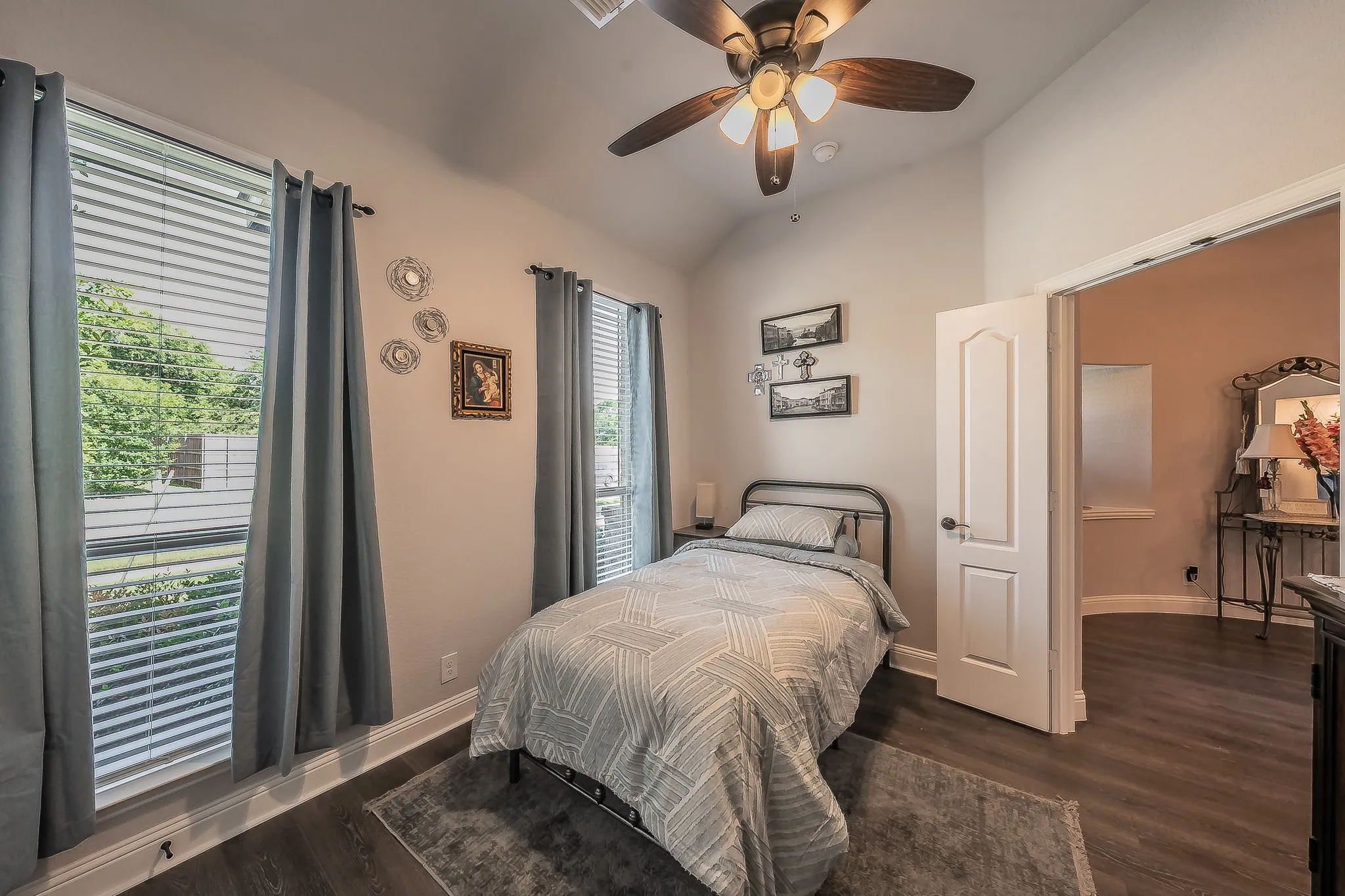 Interior room with wood-finish flooring, two large windows with blinds, a ceiling fan with integrated lighting, and a vaulted ceiling