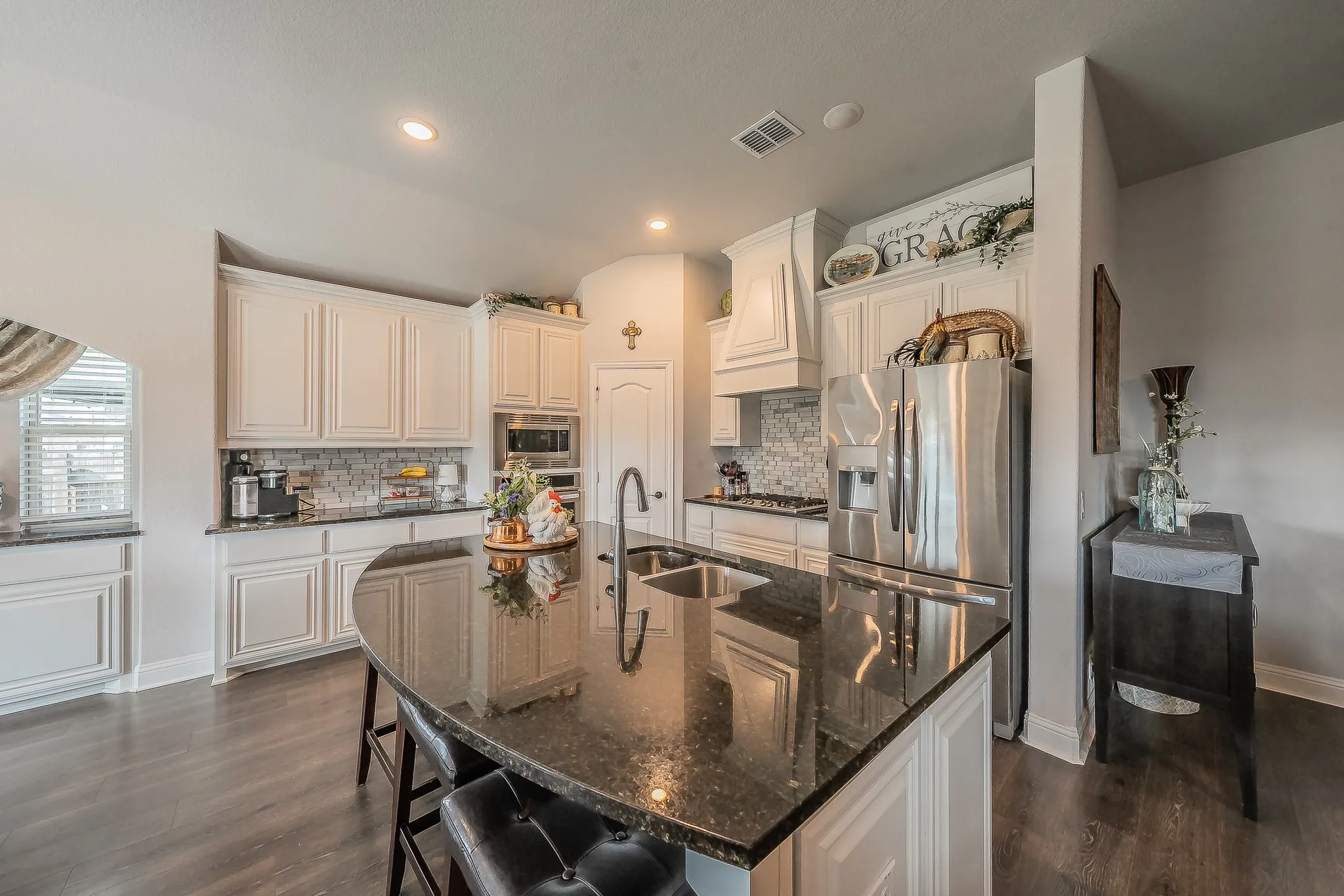 Kitchen featuring a large island with dark stone countertop, white cabinetry with crown molding, stainless steel appliances, tile backsplash, and wood-finish flooring