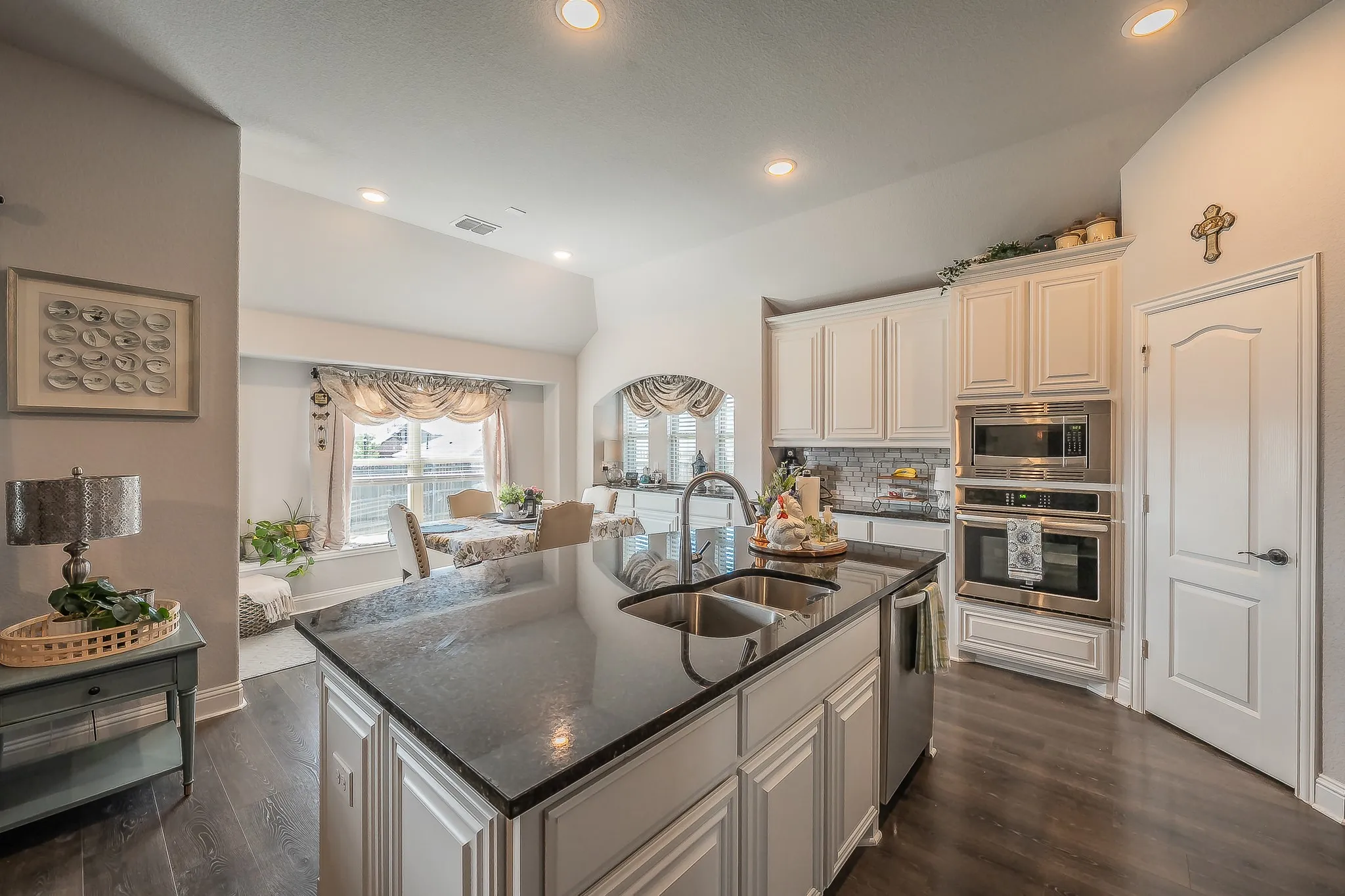 Kitchen featuring a large island with an undermount double-basin sink, dark stone countertop, white cabinetry, integrated stainless steel appliances, and wood-finish flooring