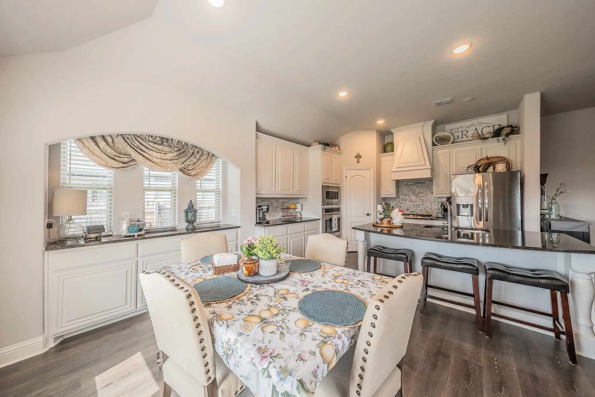 Open-concept kitchen and dining area featuring wood-finish flooring, white cabinetry, a large kitchen island with bar seating, and a built-in buffet with an arched opening