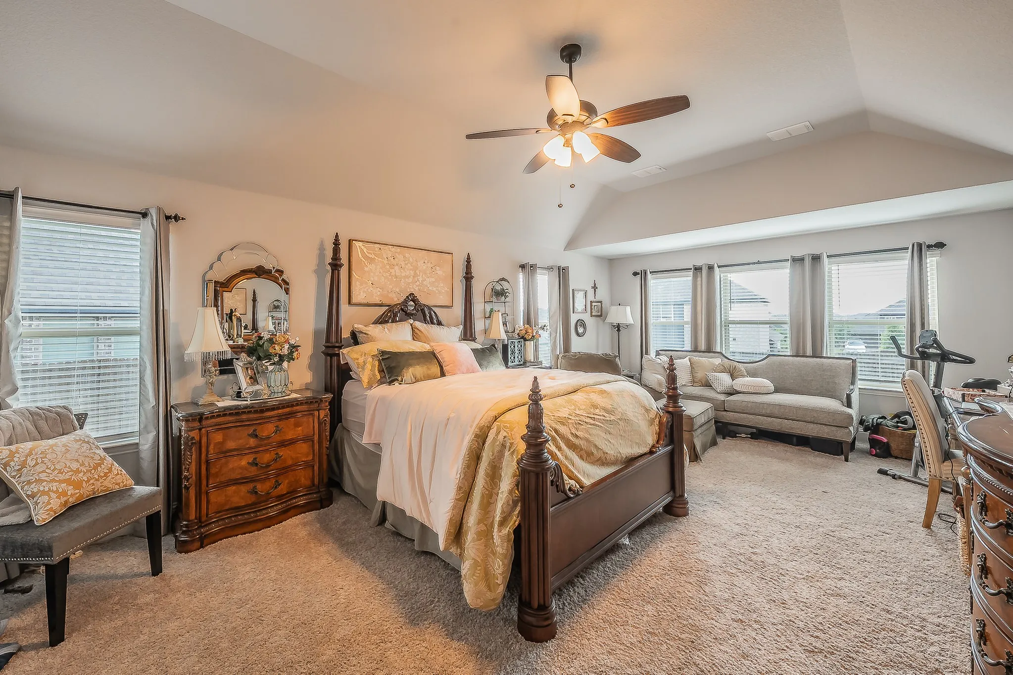 Spacious room featuring vaulted ceilings, a ceiling fan, multiple windows with blinds, and neutral carpeting