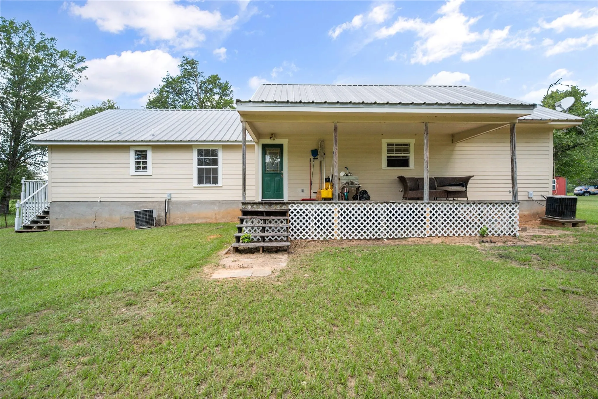 Rear view of farmhouse with covered porch, metal roof, fenced yard, and peaceful 42-acre setting.
