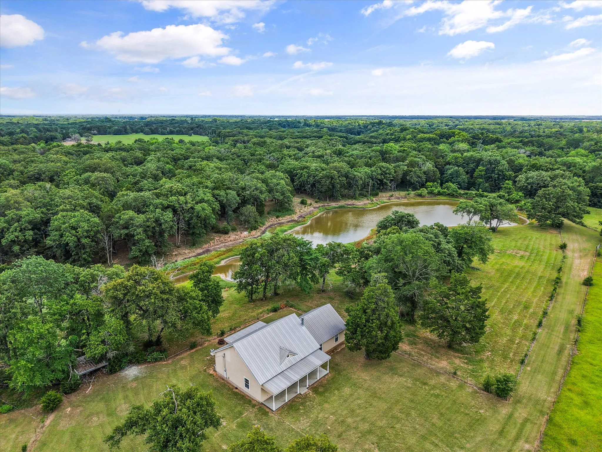 Aerial view of farmhouse, pond, trees, and pasture on a scenic 42-acre Navarro County property.