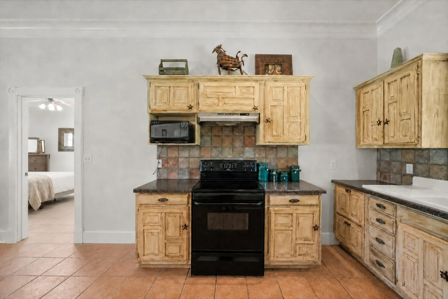 Rustic farmhouse kitchen with neutral bedroom view highlights the warm country character of this 42-acre Kerens TX ranch home.