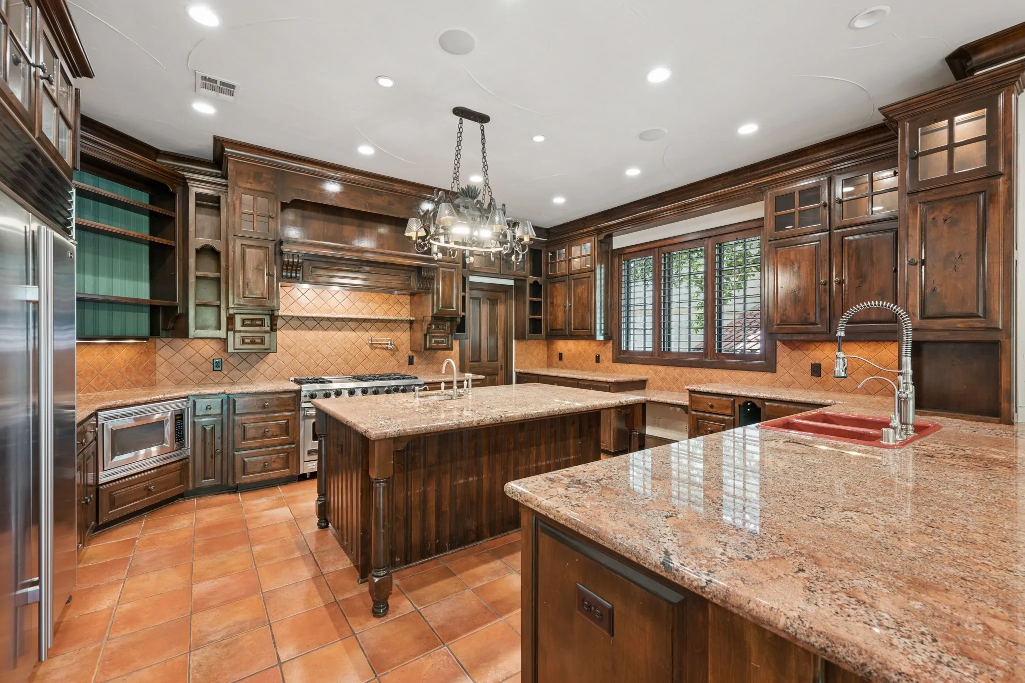 Kitchen featuring two islands with stone countertops, terracotta tile flooring, and dark wood cabinetry with integrated appliances