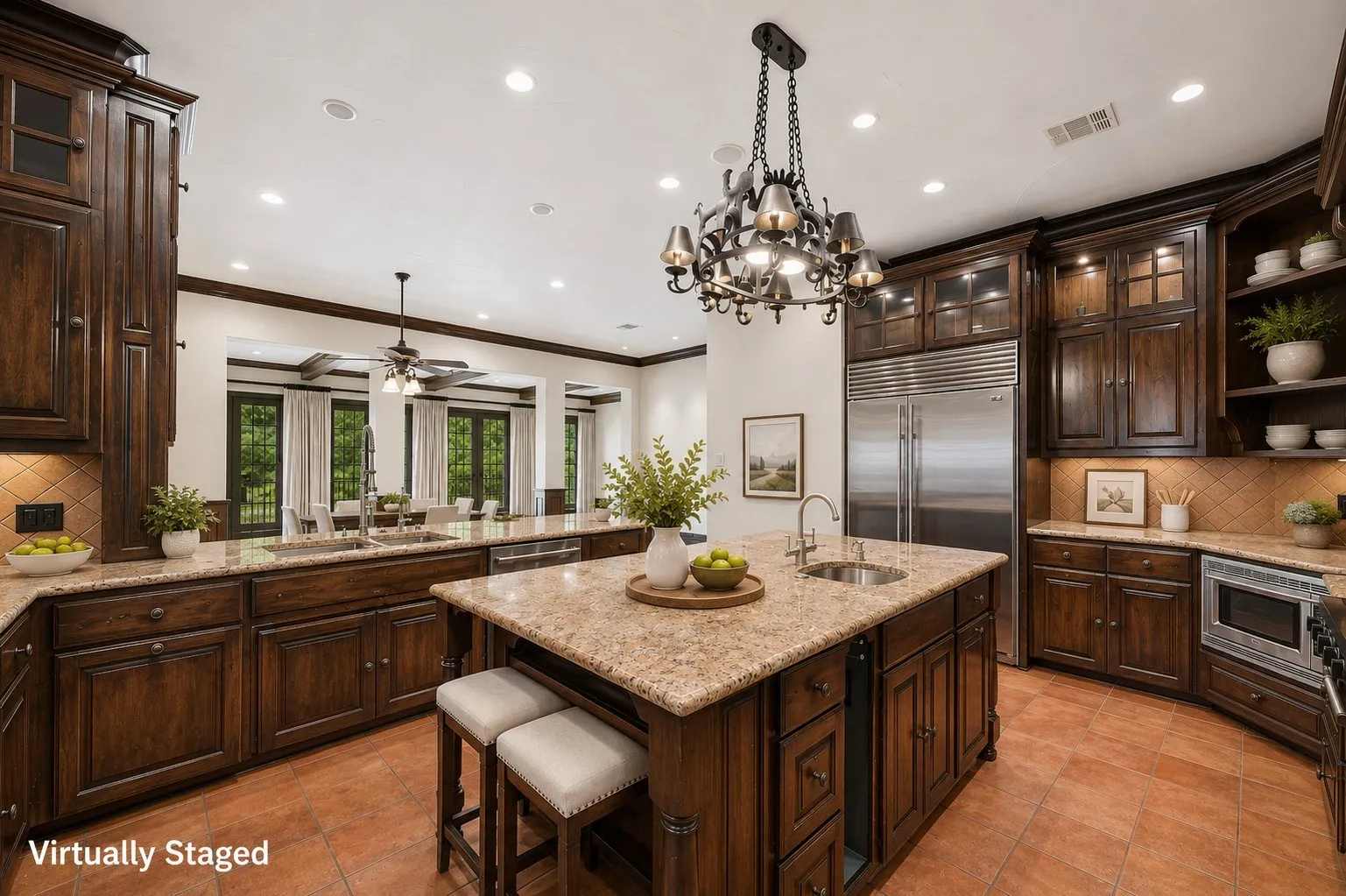 Kitchen featuring a large central island with seating, stainless steel appliances, dark wood cabinetry with crown molding, light-toned granite countertops, and terracotta-style flooring