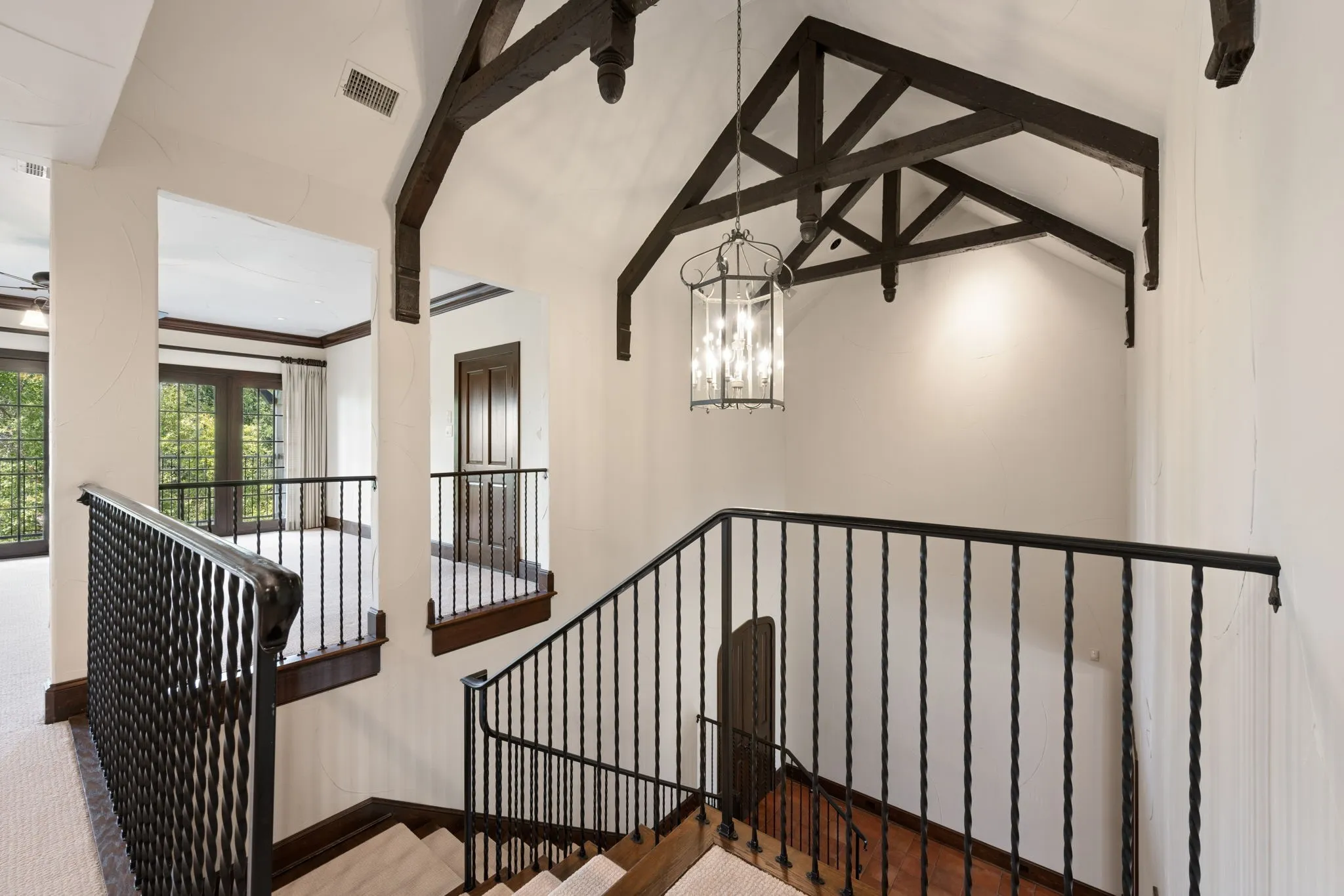 Staircase featuring dark wood handrails with intricate wrought iron balusters and chandelier that raises and lowers