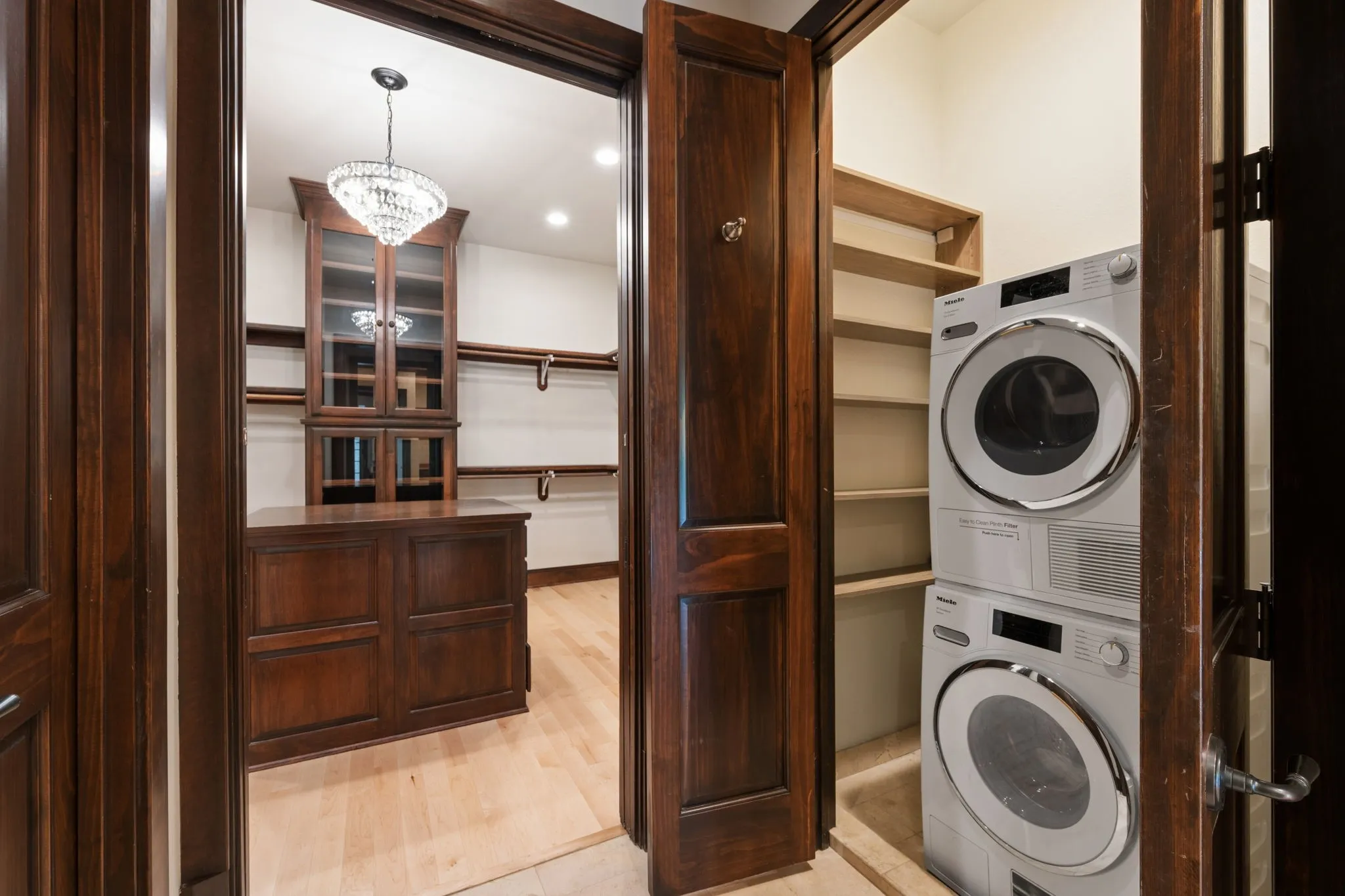 Custom closet with a central wood-finish island, built-in cabinetry with glass doors, and a decorative chandelier
