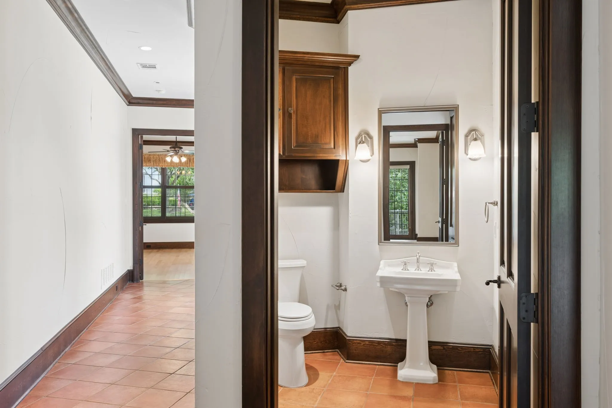 Powder room featuring a pedestal sink with a chrome faucet, wall-mounted mirror, and sconce lighting