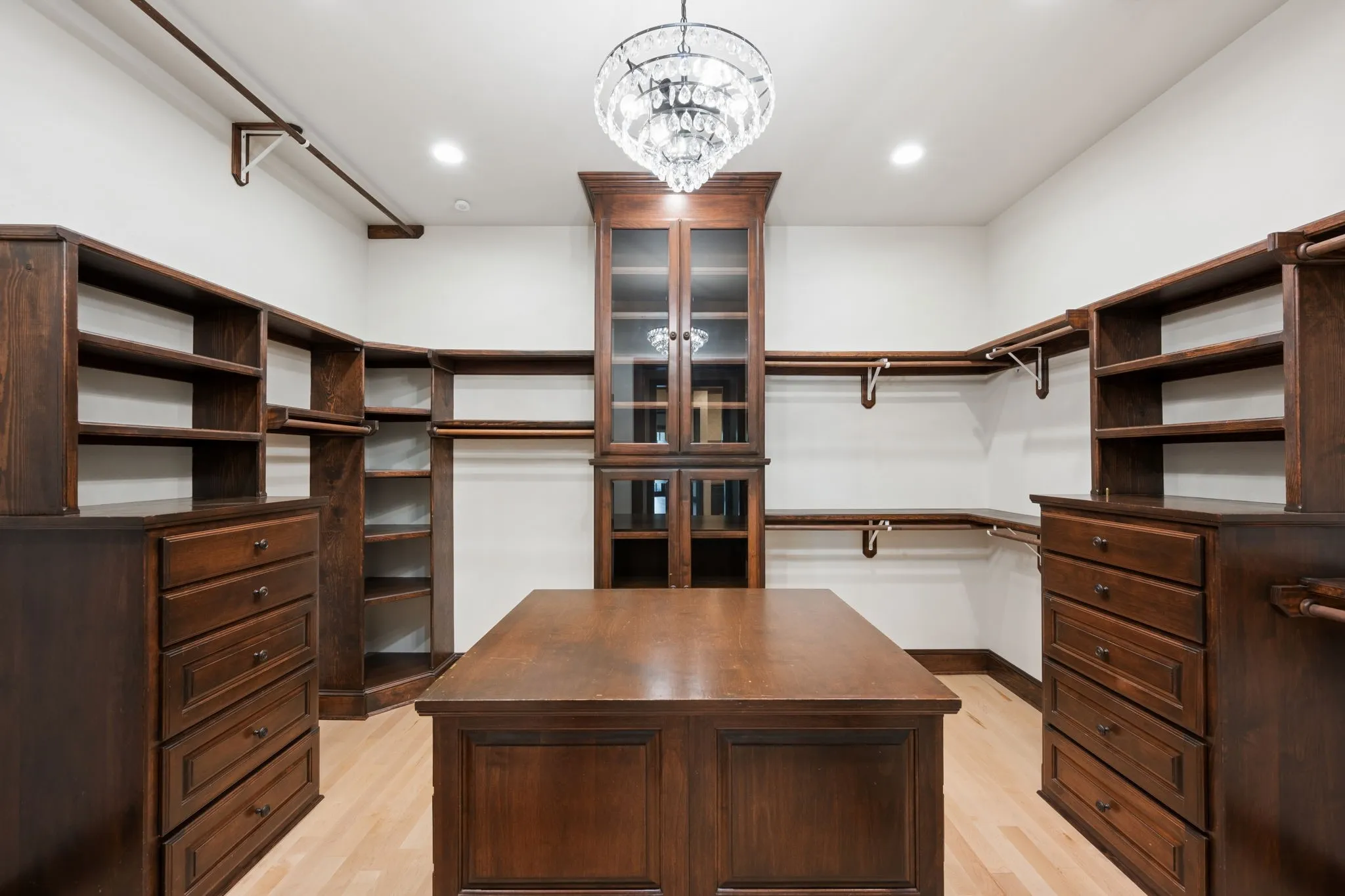 Primary bathroom custom-designed walk-in closet featuring extensive dark wood-finish cabinetry, a central island with storage, and a crystal chandelier