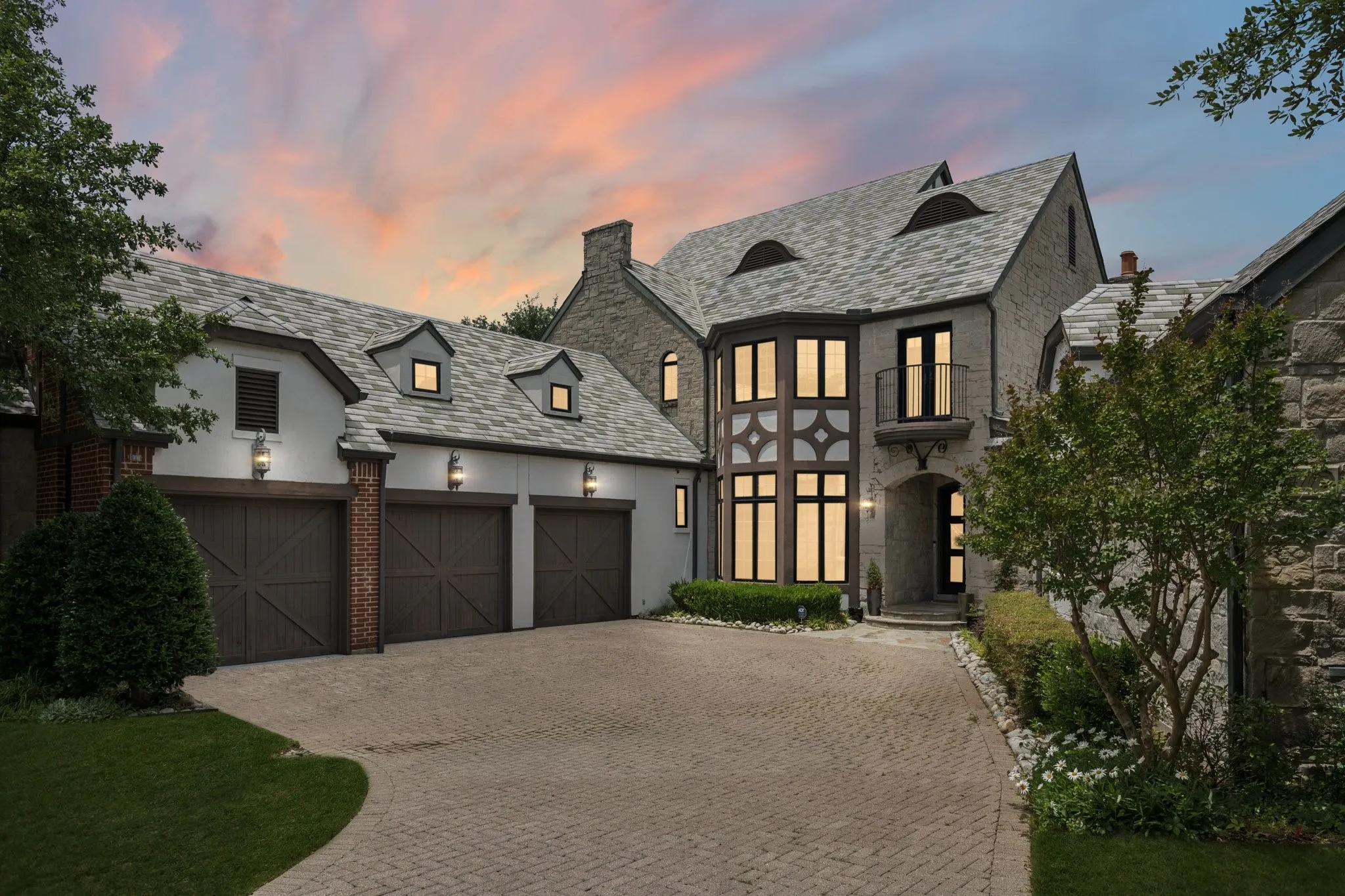 Stone and stucco facade residence featuring a multi-gable roofline, three dormer windows, and an arched entry