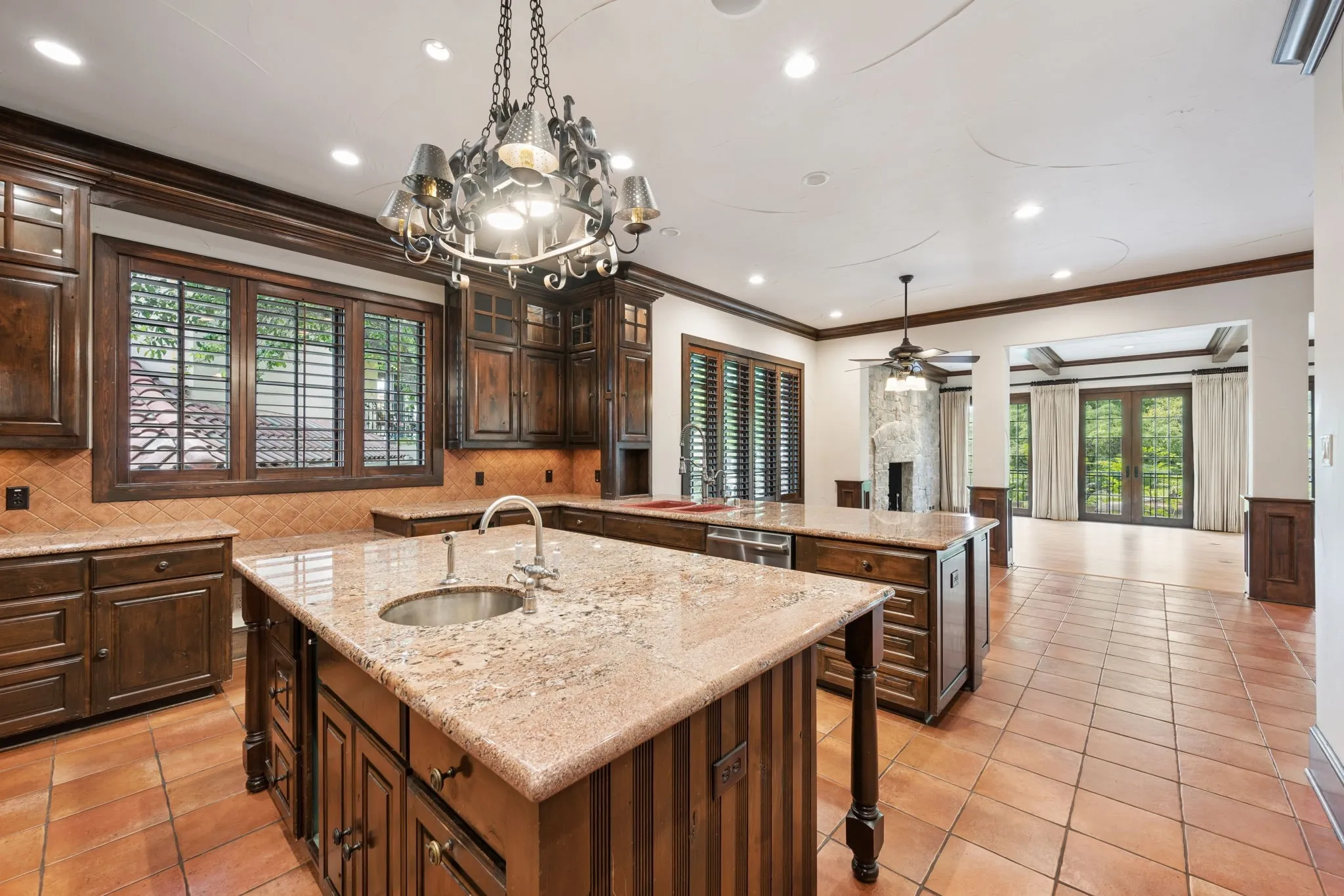 Kitchen featuring two large islands with stone countertops, a double basin sink with a gooseneck faucet, dark wood cabinetry, and terracotta tile flooring