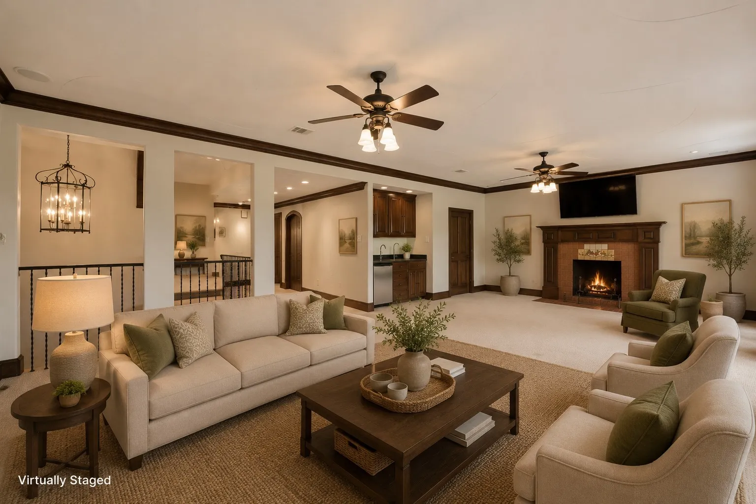 Spacious living area featuring a prominent fireplace with an ornate wood mantel, multiple ceiling fans, a built-in wet bar with stainless steel appliances, and a wrought iron banister