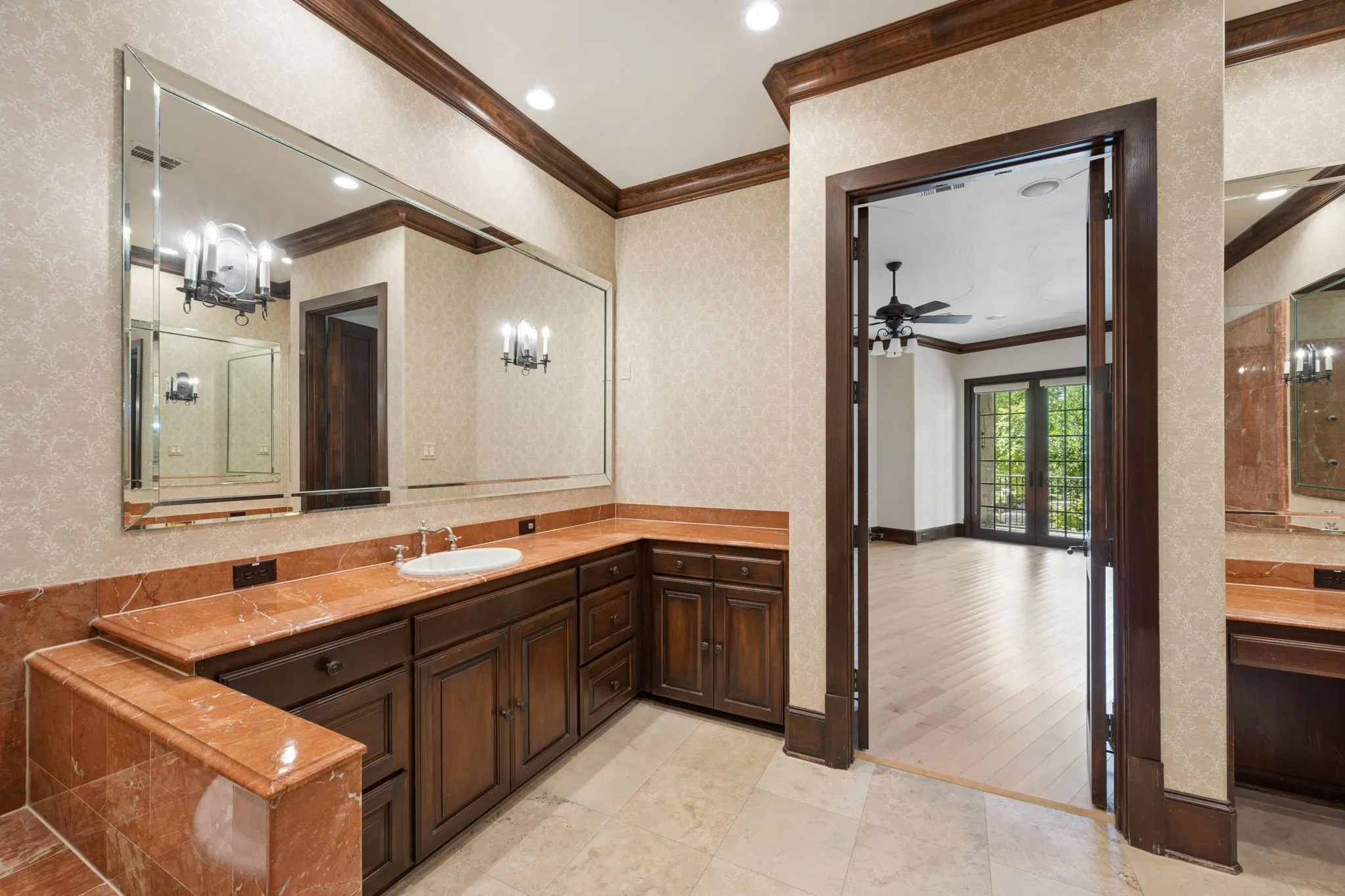 Vanity area with a single undermount sink set into a red-toned countertop, featuring rich wood cabinetry and a large wall-mounted mirror