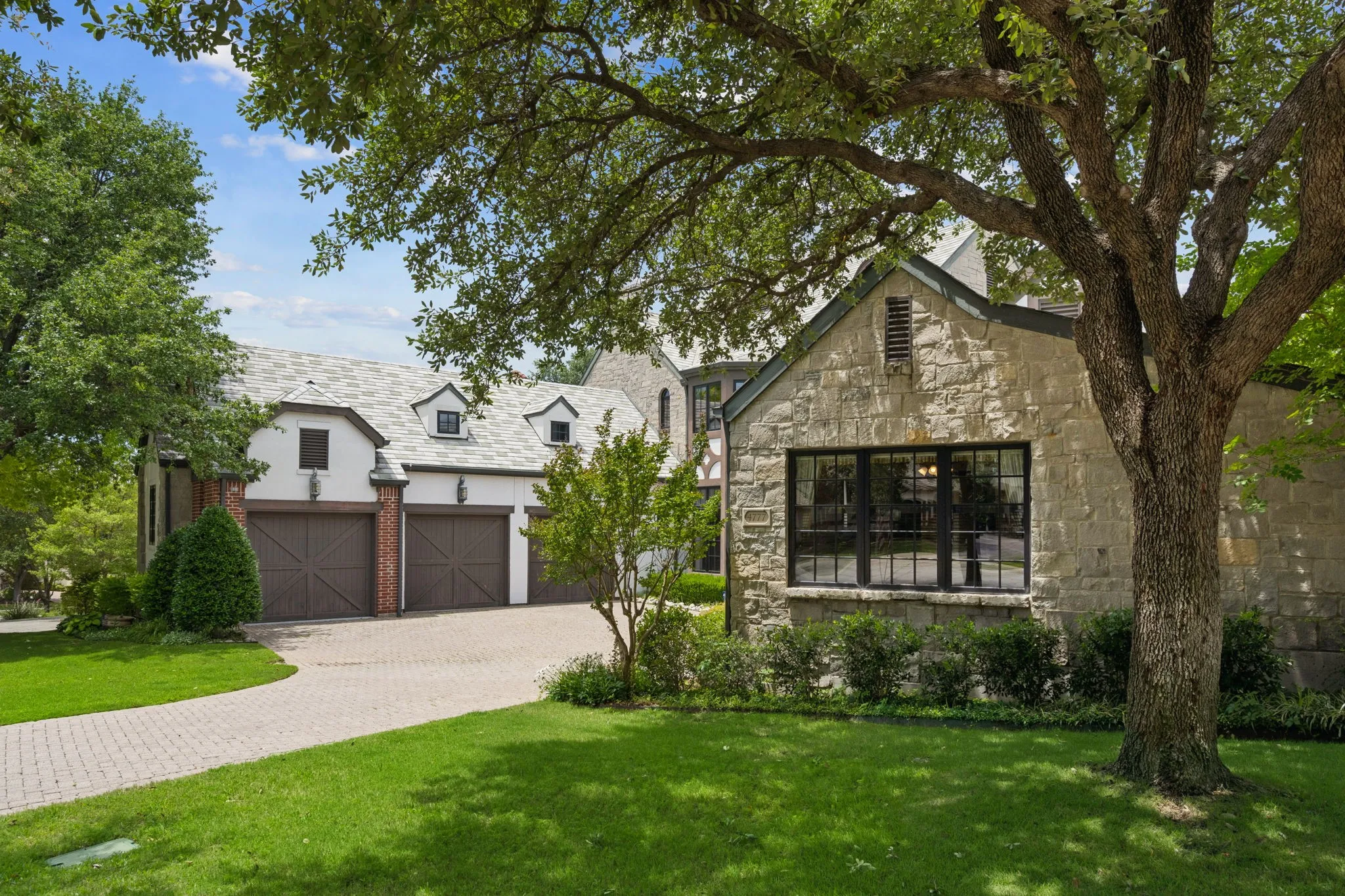 Stone-clad exterior featuring multi-pane windows, a paver driveway, and a three-car garage with carriage-style doors