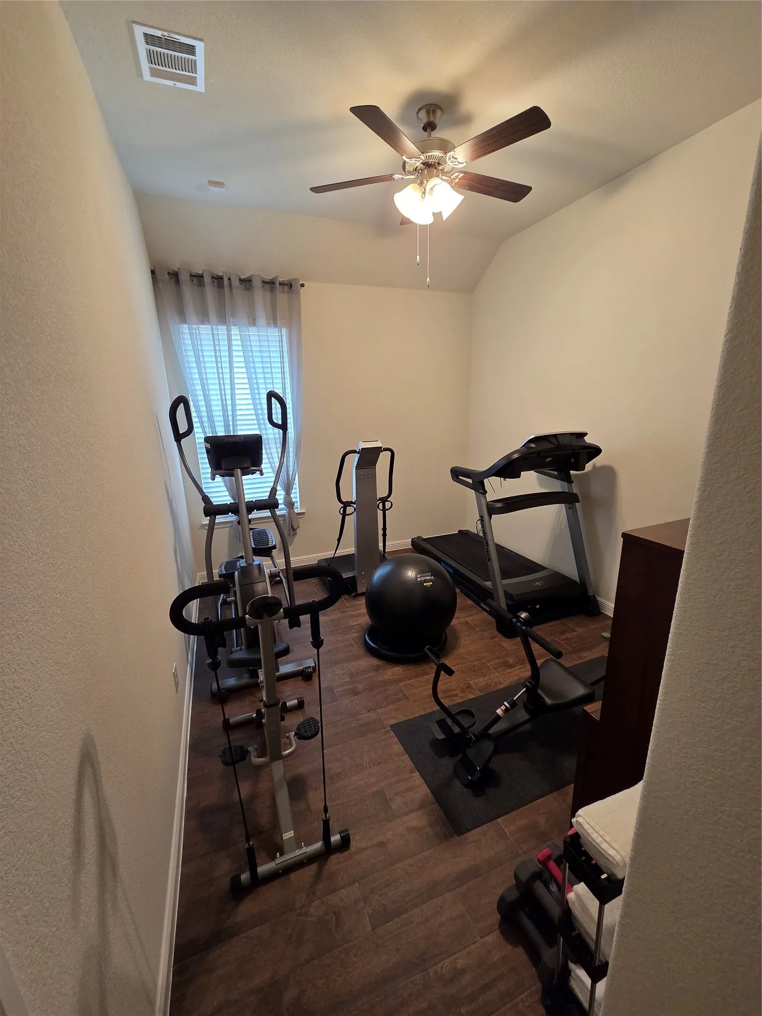 Versatile bonus room featuring wood-finish flooring, a window with horizontal blinds and curtains, and a ceiling fan with integrated lighting