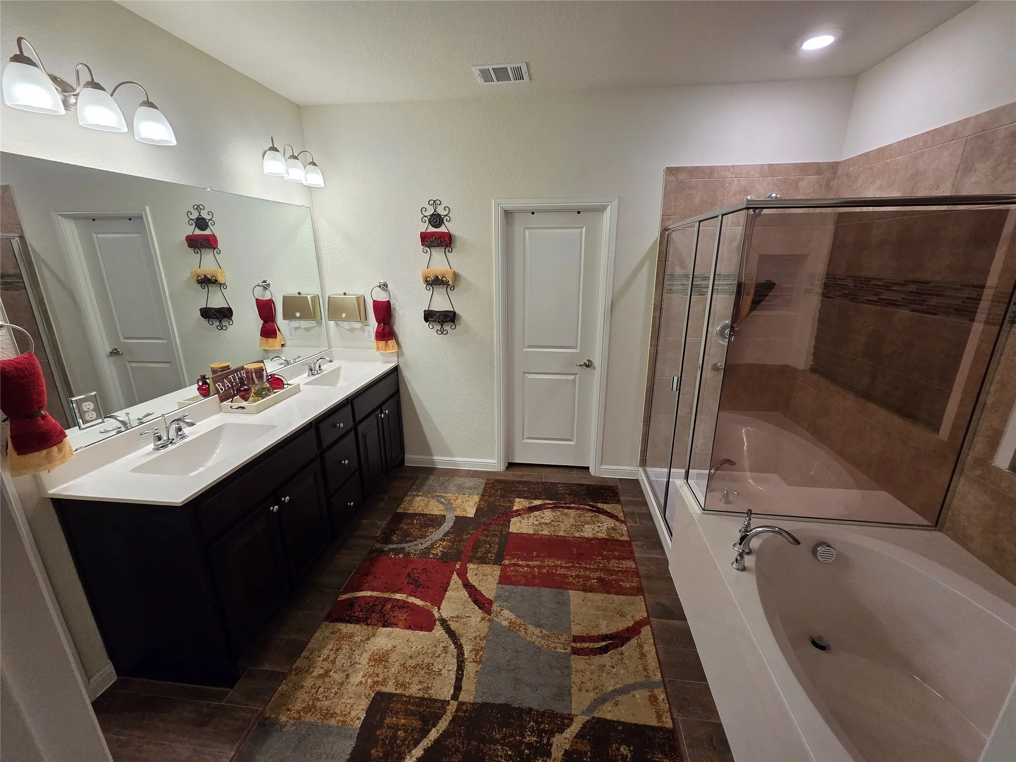 Bathroom featuring a dual vanity with white countertops, dark wood cabinetry, a large mirror, and individual light fixtures