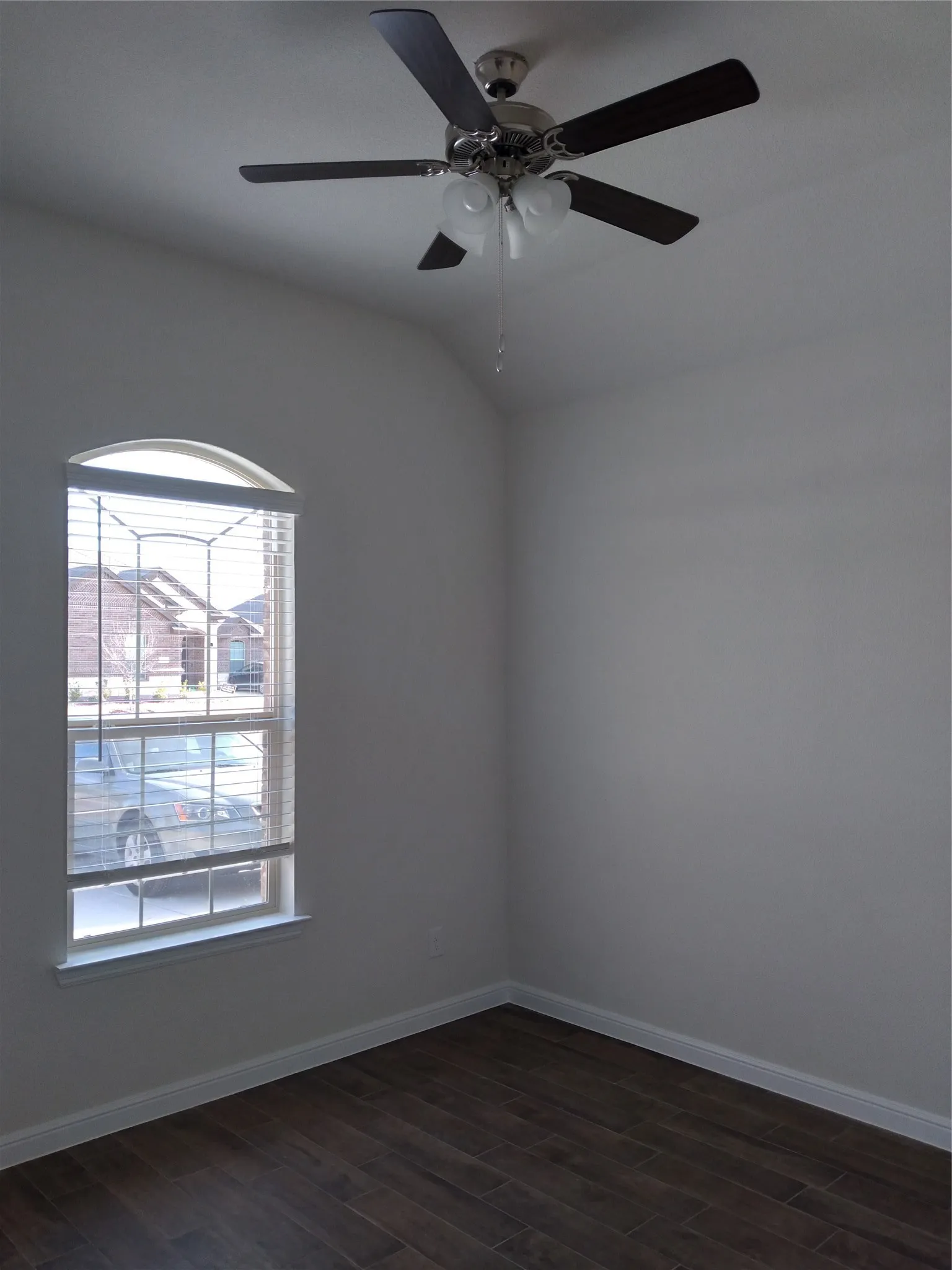Room featuring a vaulted ceiling with a ceiling fan light fixture, an arched window with horizontal blinds, wood-look plank flooring, and white baseboards