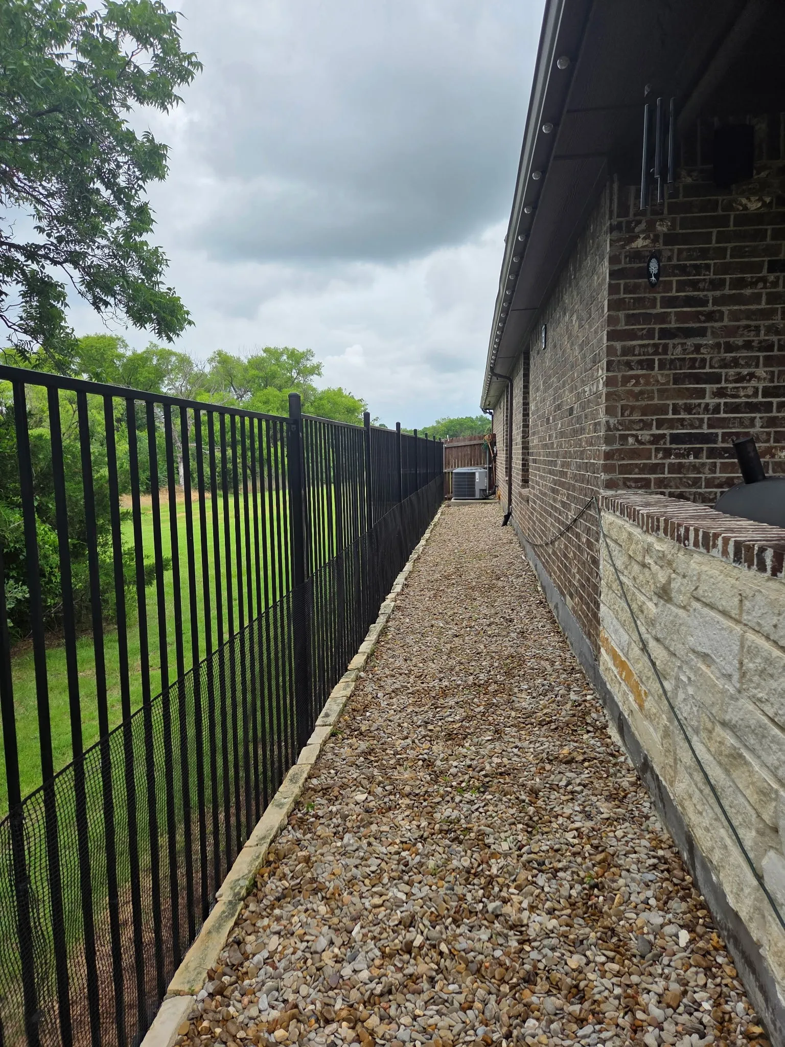 Gravel pathway bordering a brick and stone exterior with a black metal fence