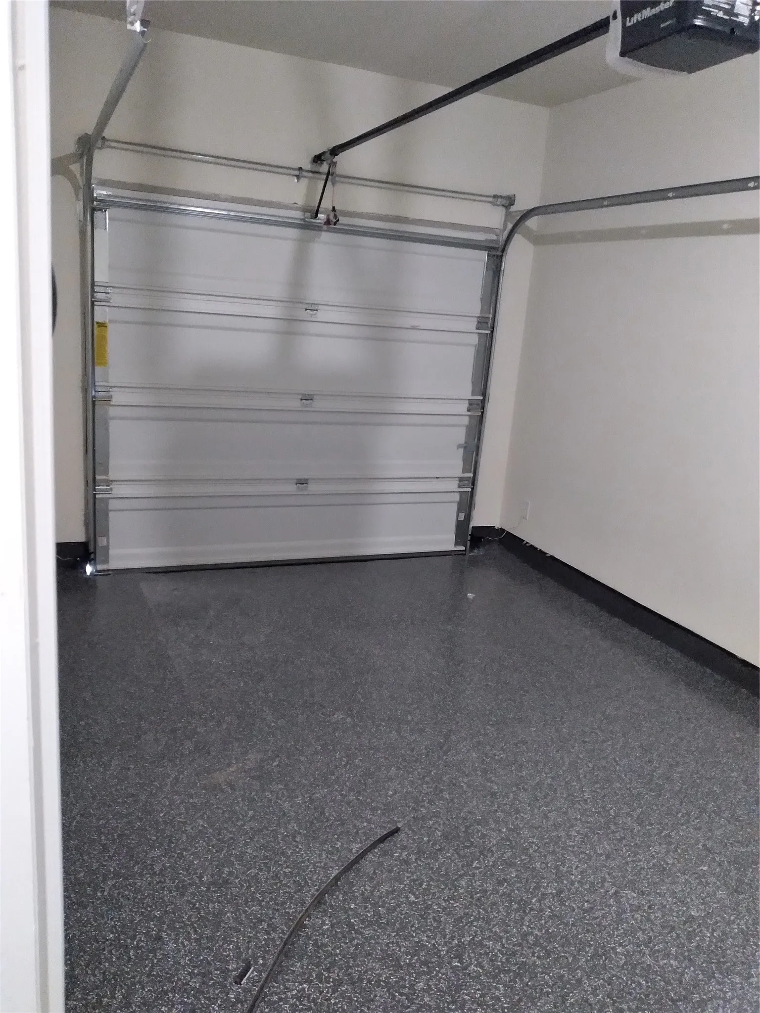 Garage interior featuring an automatic overhead door, a LiftMaster garage door opener, painted walls, and a speckled epoxy floor finish