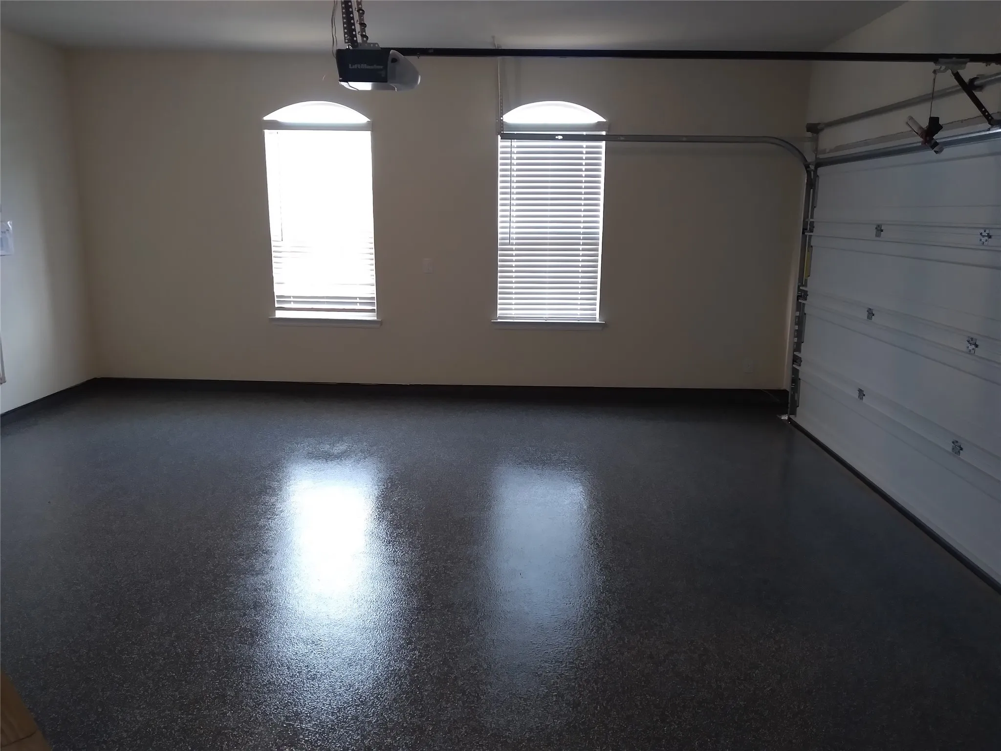 Spacious garage featuring a durable epoxy floor finish, automatic garage door opener, and two arched windows with blinds