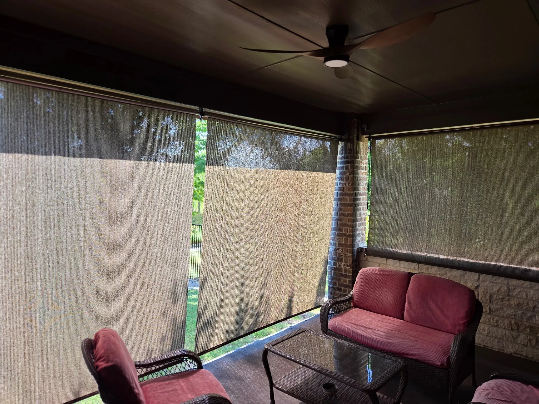 Covered patio featuring a dark wood ceiling, integrated ceiling fan with lighting, brick columns, and privacy shades