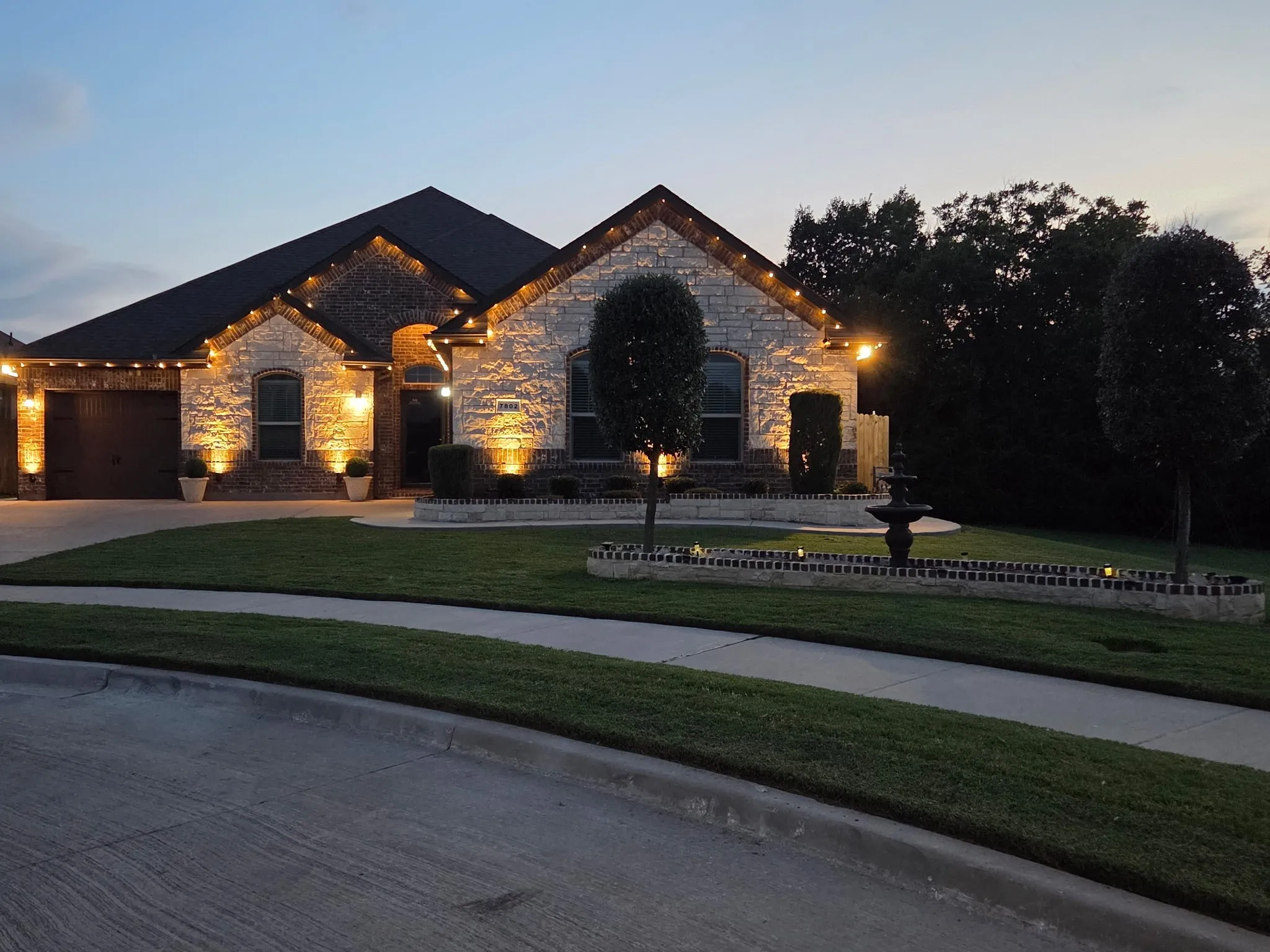 Stone and brick veneer exterior featuring a two-car garage, arched entry, and extensive landscape lighting