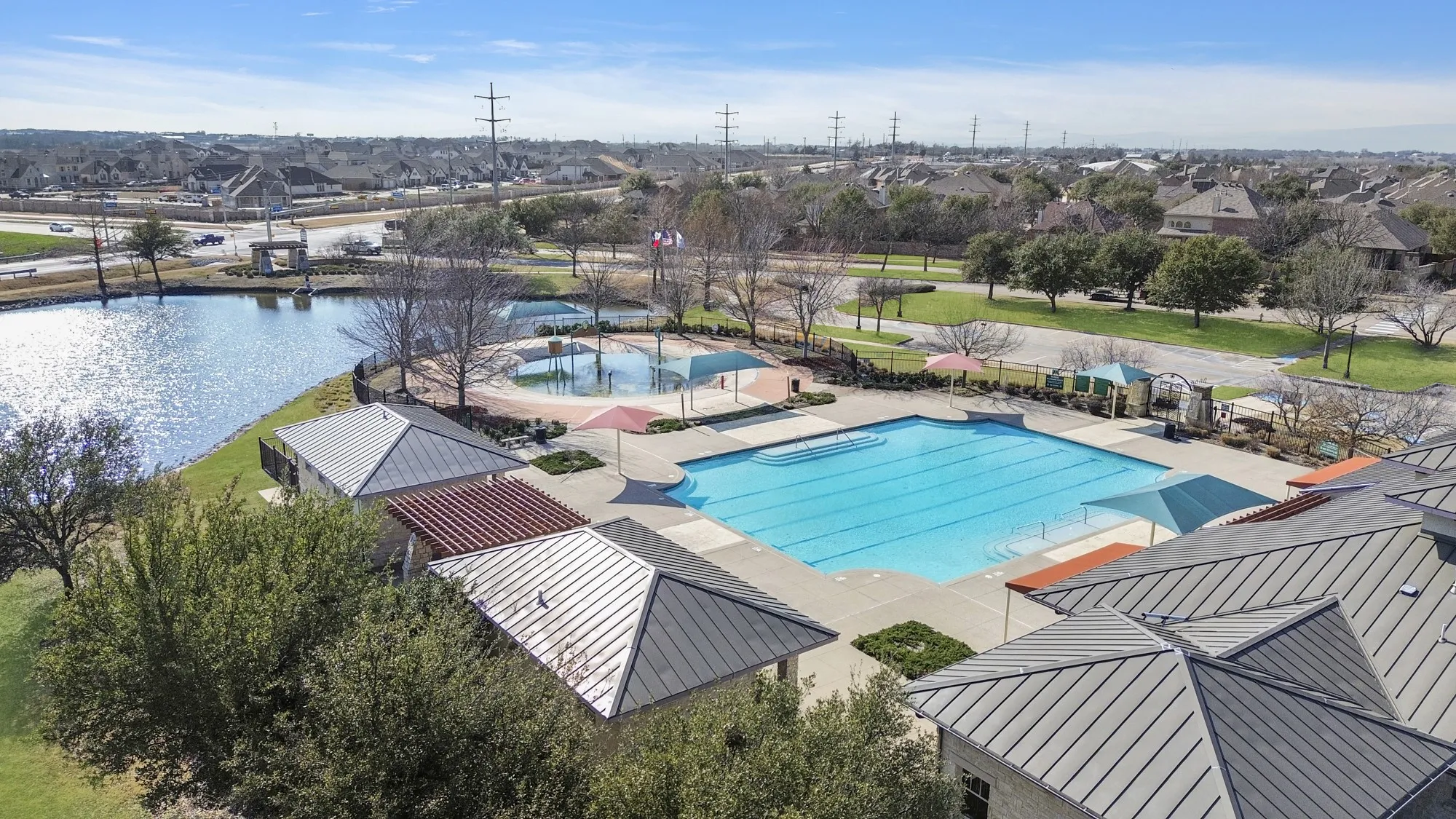 Community amenities featuring a large outdoor swimming pool with lap lanes, a shallow water play area, surrounding concrete decking, and covered shade structures