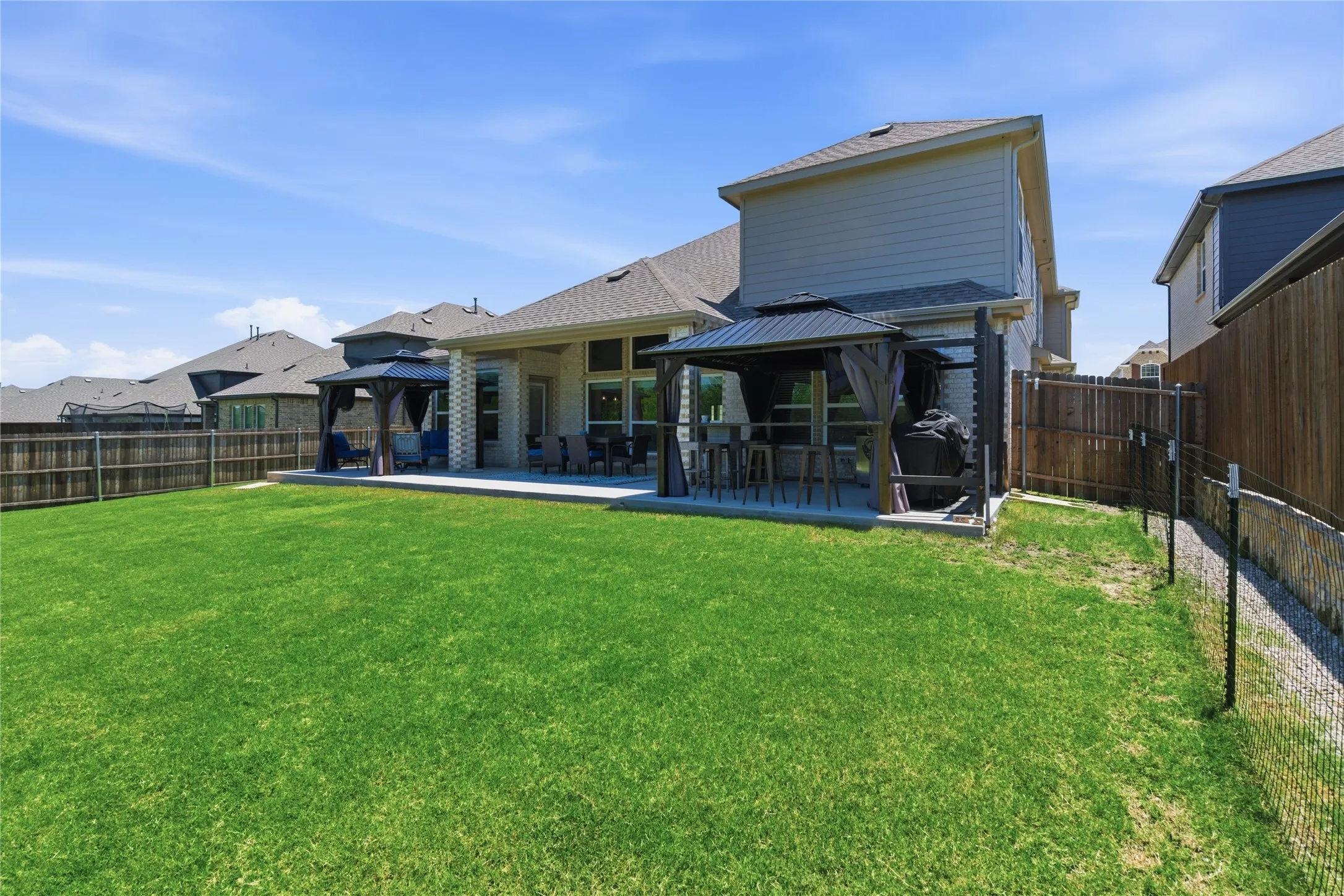 Spacious backyard featuring a large concrete patio, two covered gazebos, and a privacy fence
