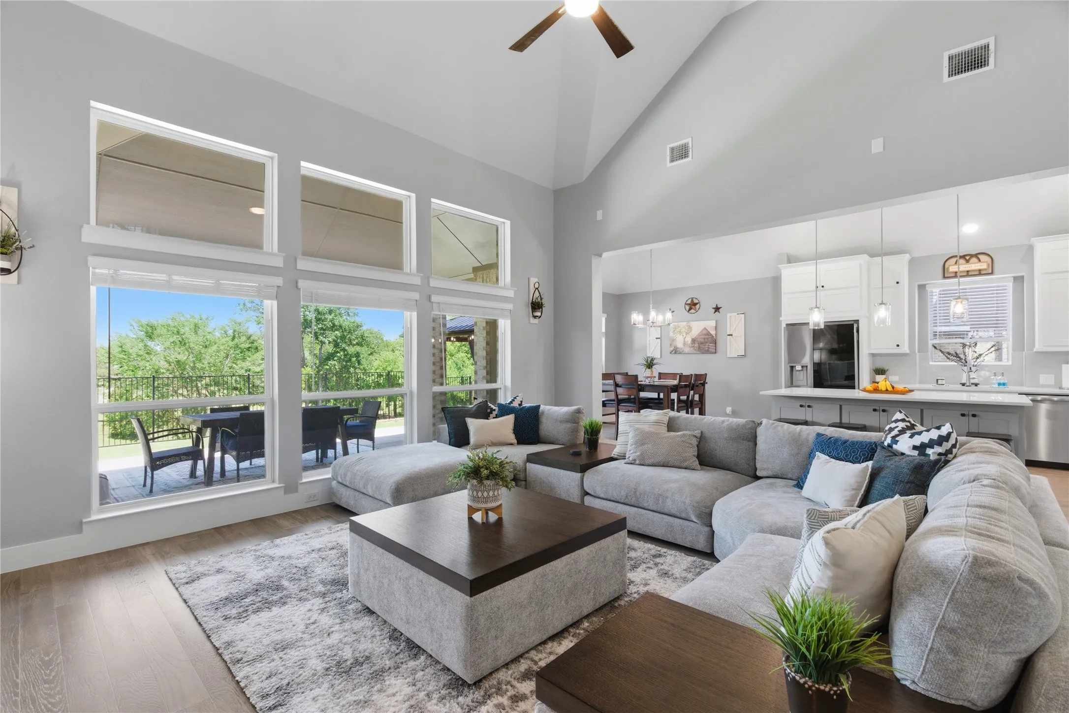Great room featuring vaulted ceilings, wood-finish flooring, a contemporary ceiling fan, and a wall of windows overlooking an outdoor patio