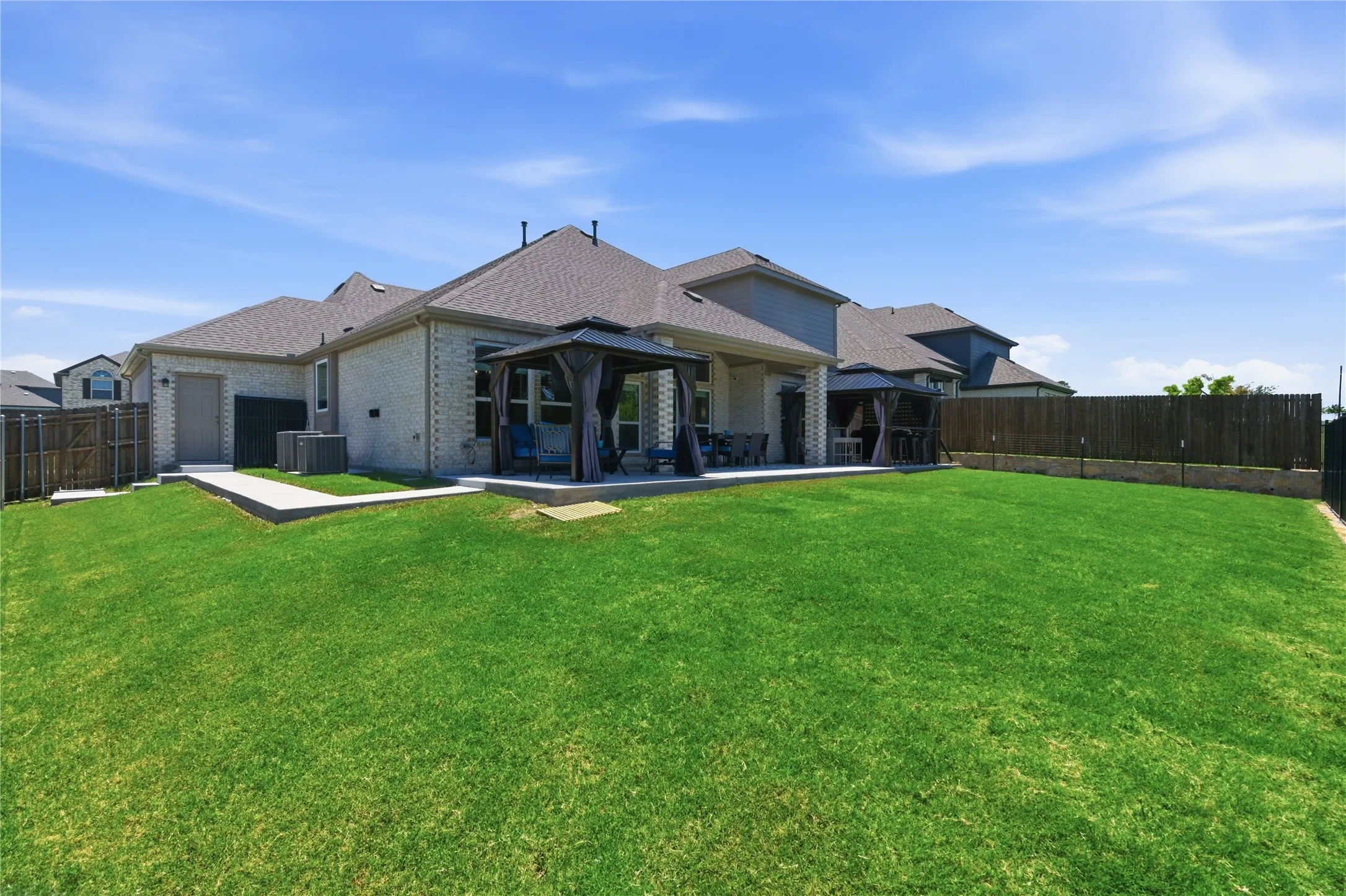 Spacious backyard featuring an expansive lawn, a covered patio with an outdoor gazebo, and a privacy fence