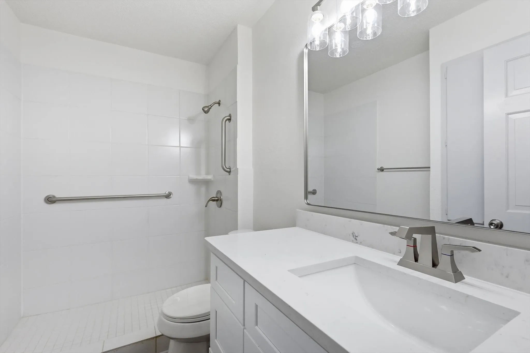 Bathroom featuring a white subway tile shower, white vanity with integrated sink, stone-finish countertop, brushed nickel faucet, and a large wall-mounted mirror with overhead lighting