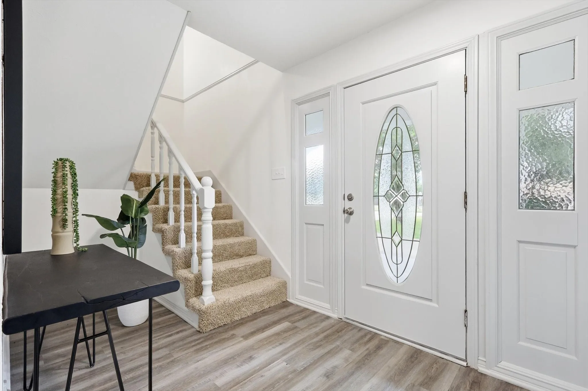 Entryway featuring a decorative glass front door with sidelights, wood-finish flooring, and a carpeted staircase with white balusters