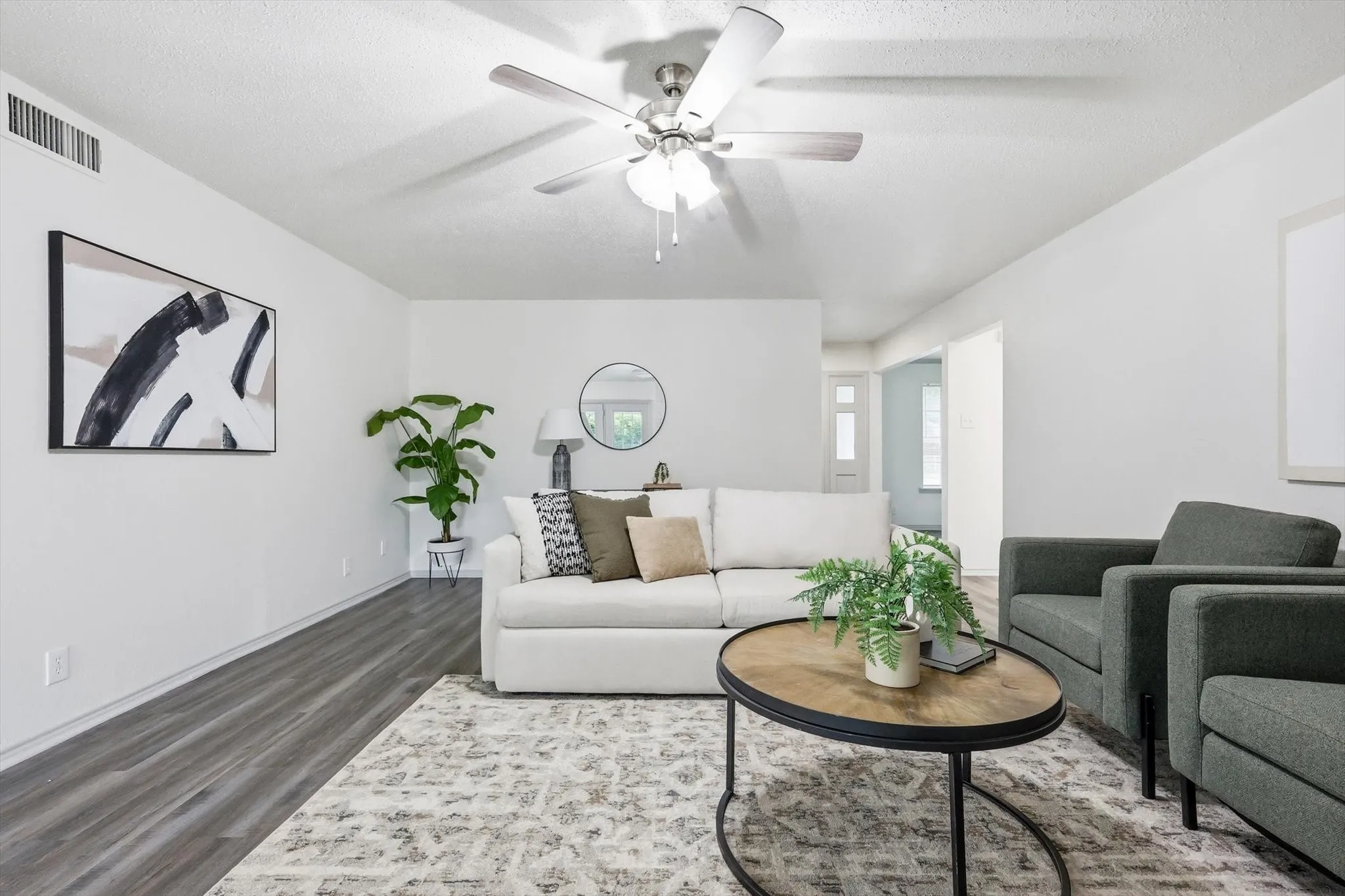 Spacious living area featuring light gray wood-finish flooring, a ceiling fan with light fixture, and white wall finishes