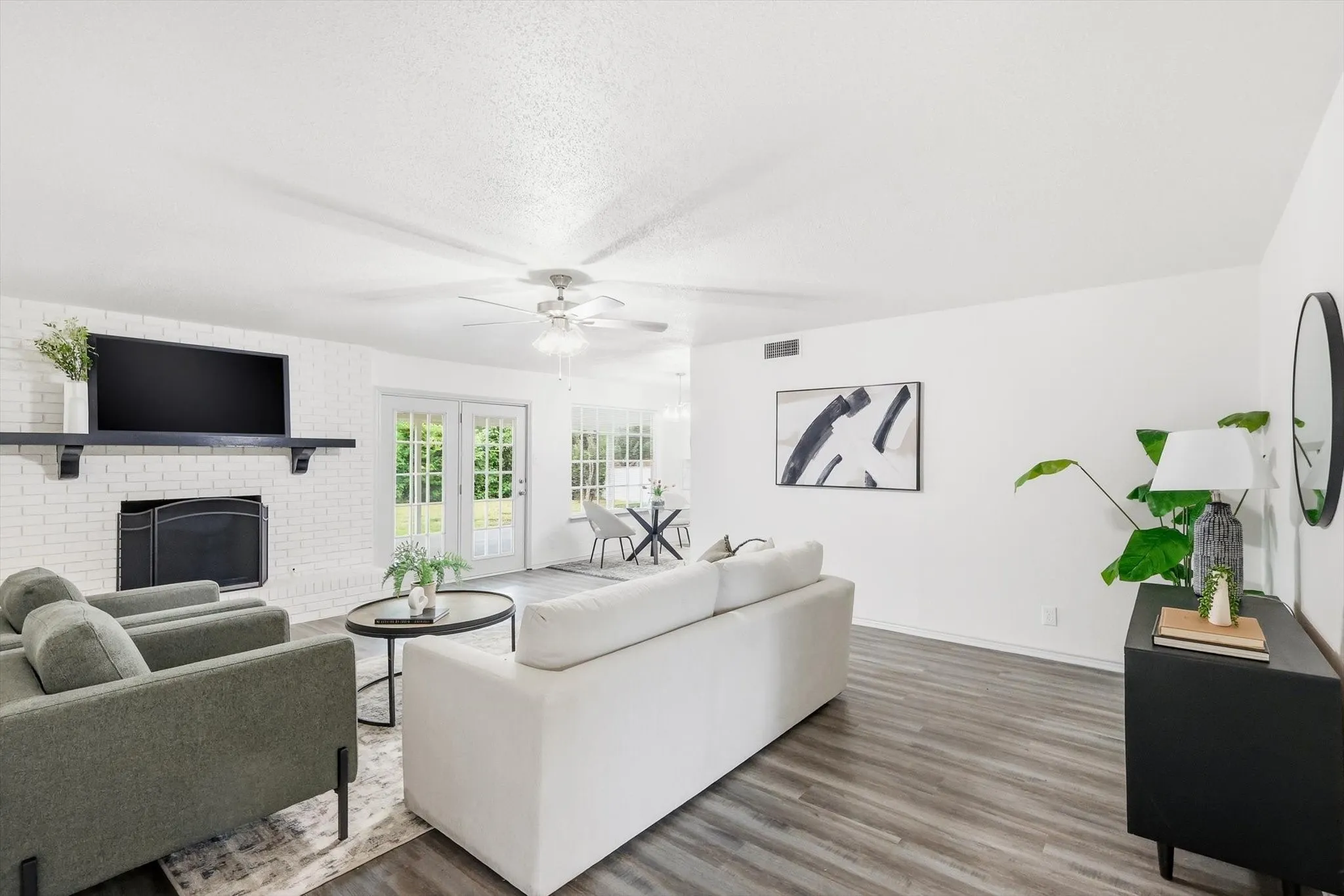 Bright living area featuring wood-finish flooring and a white brick fireplace with a black mantel